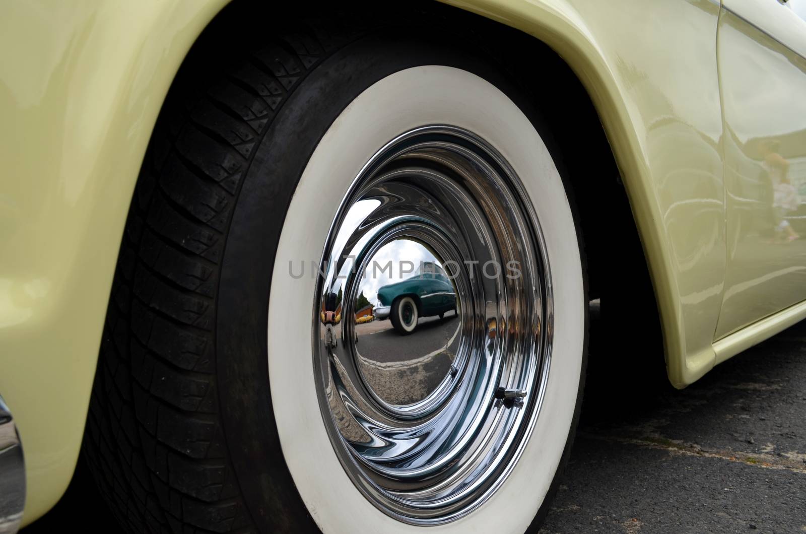 Custom car being reflected in another hotrods wheel hubcaps at a hotrod show in England.