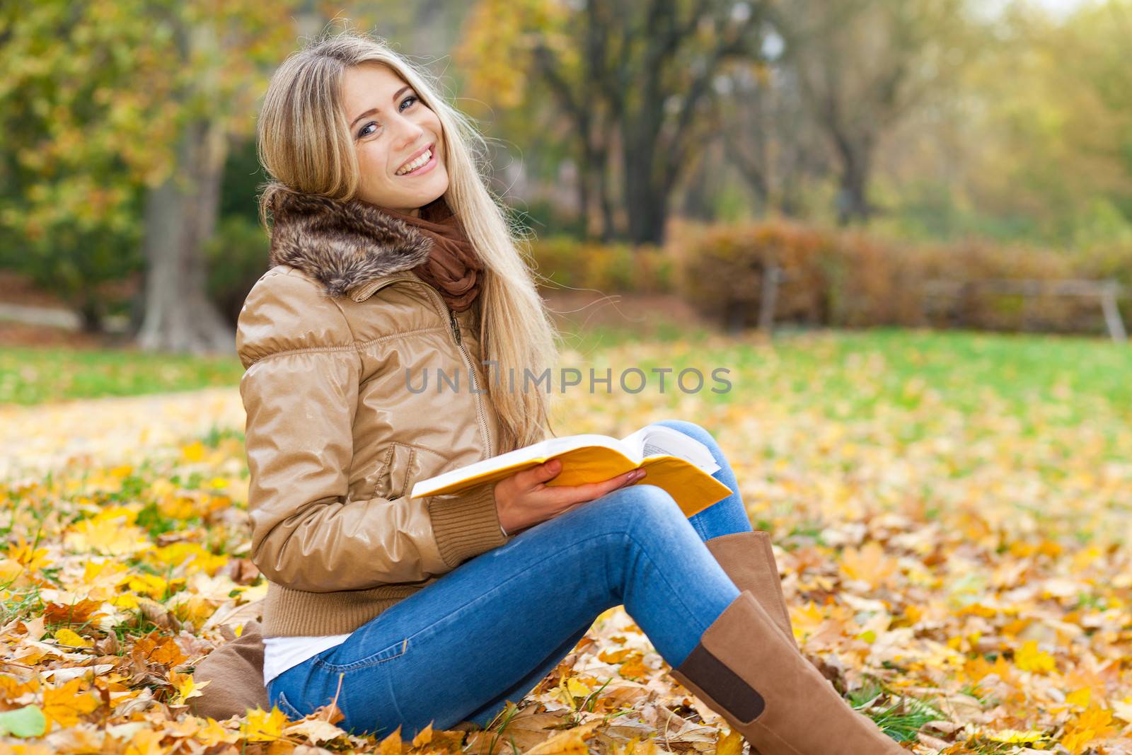 Young woman sitting in a park, holding a book and smiling