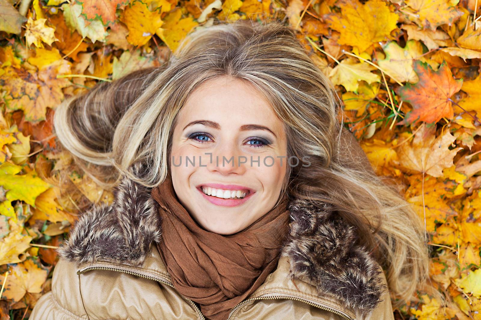 Closeup portrait of a young smiling woman surrounded by autumn leaves