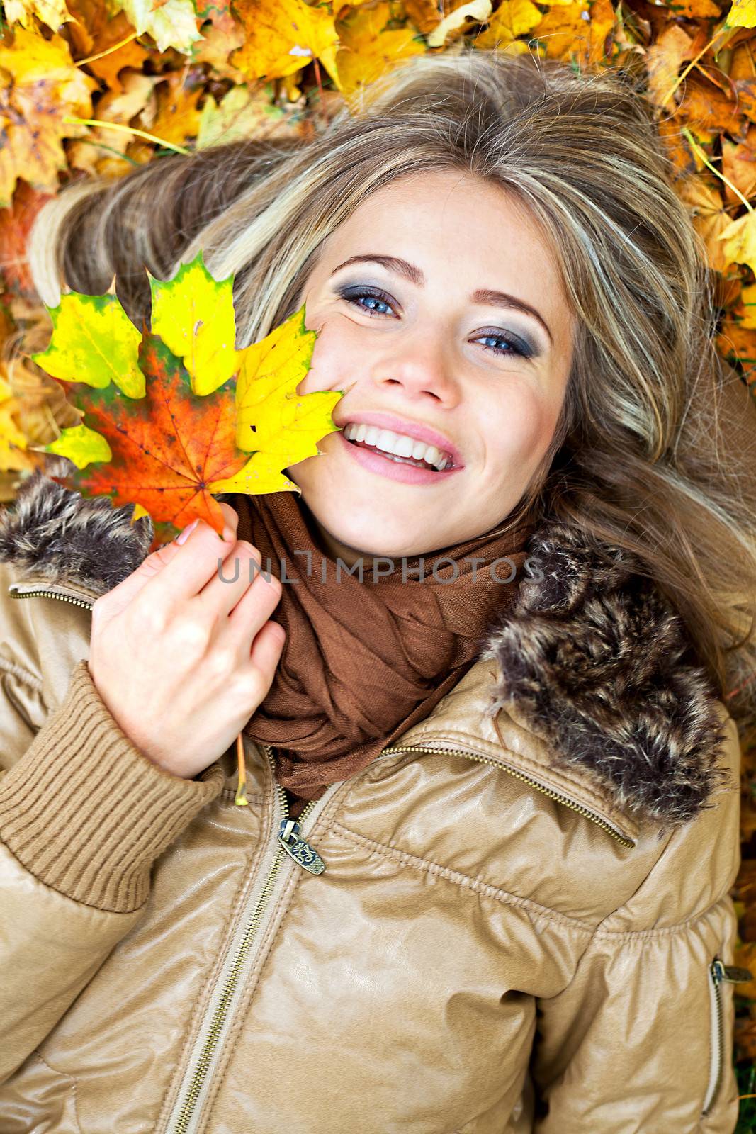 Closeup portrait of a young blond woman surrounded by autumn leaves