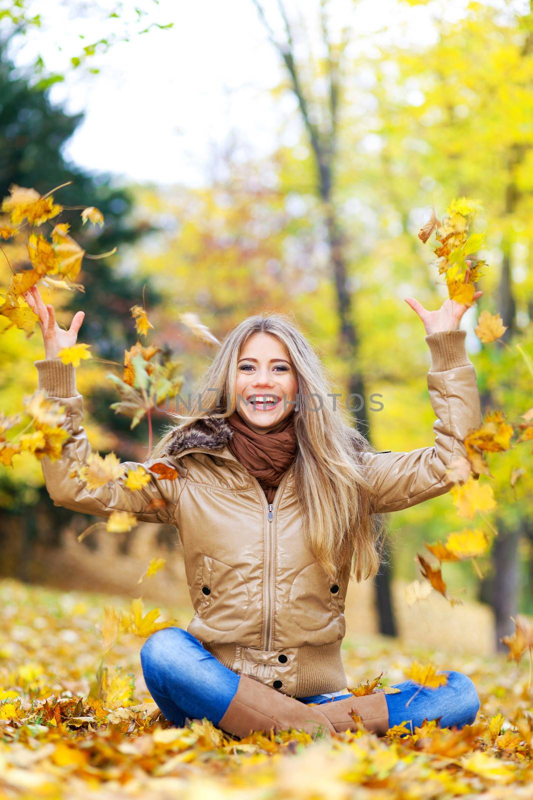 Young woman sitting in a park and throwing autumn leaves