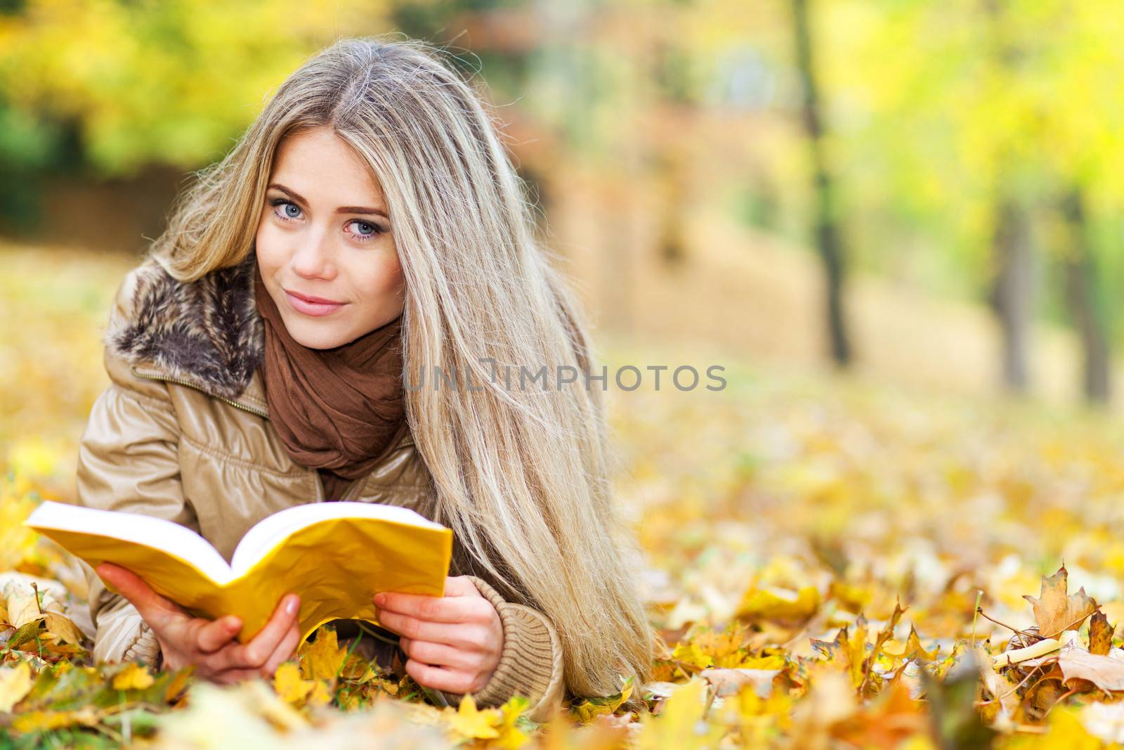 Pretty young woman reading in a park in autumn by TristanBM