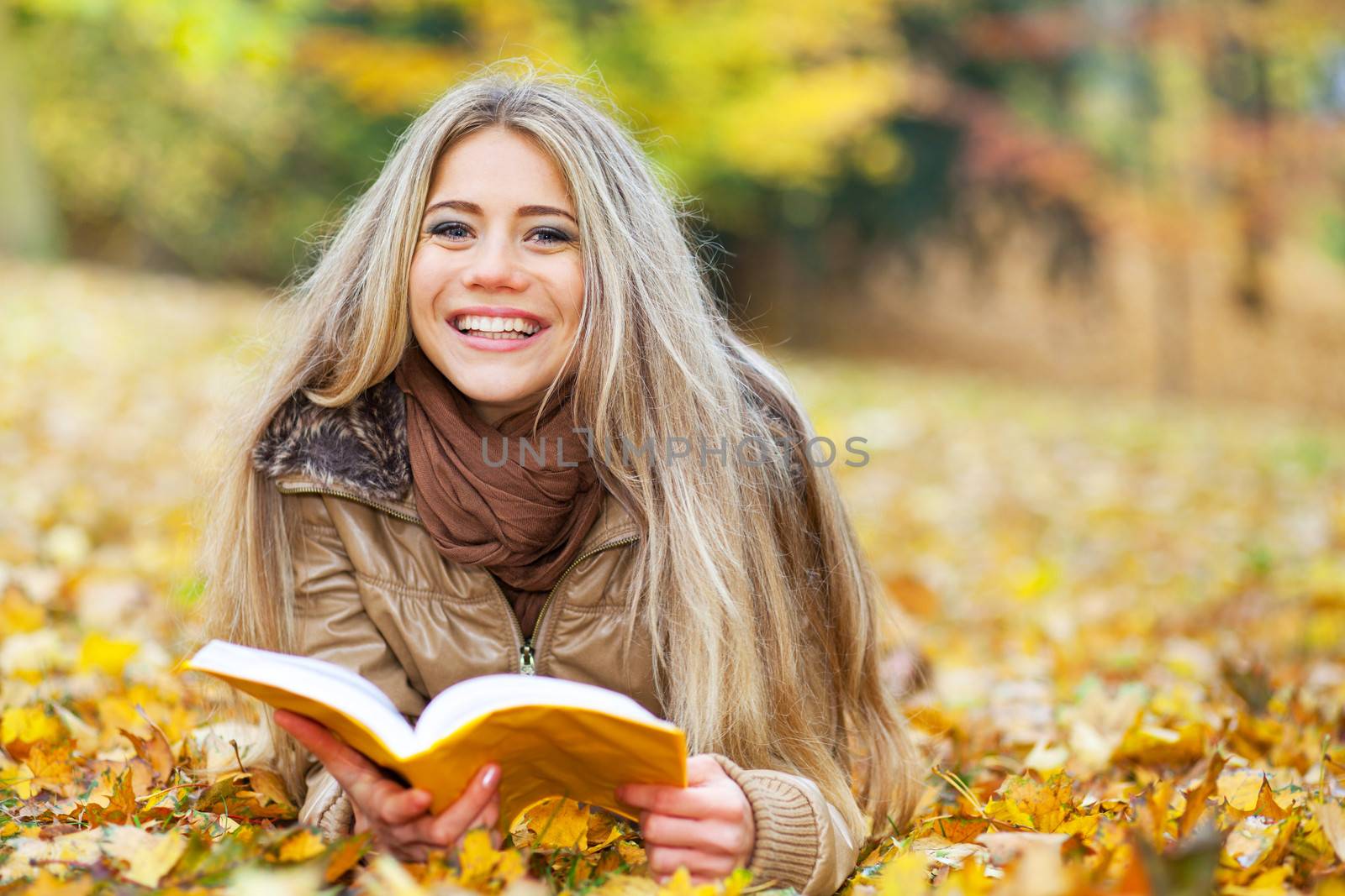 Pretty woman lying in a park, reading and smiling
