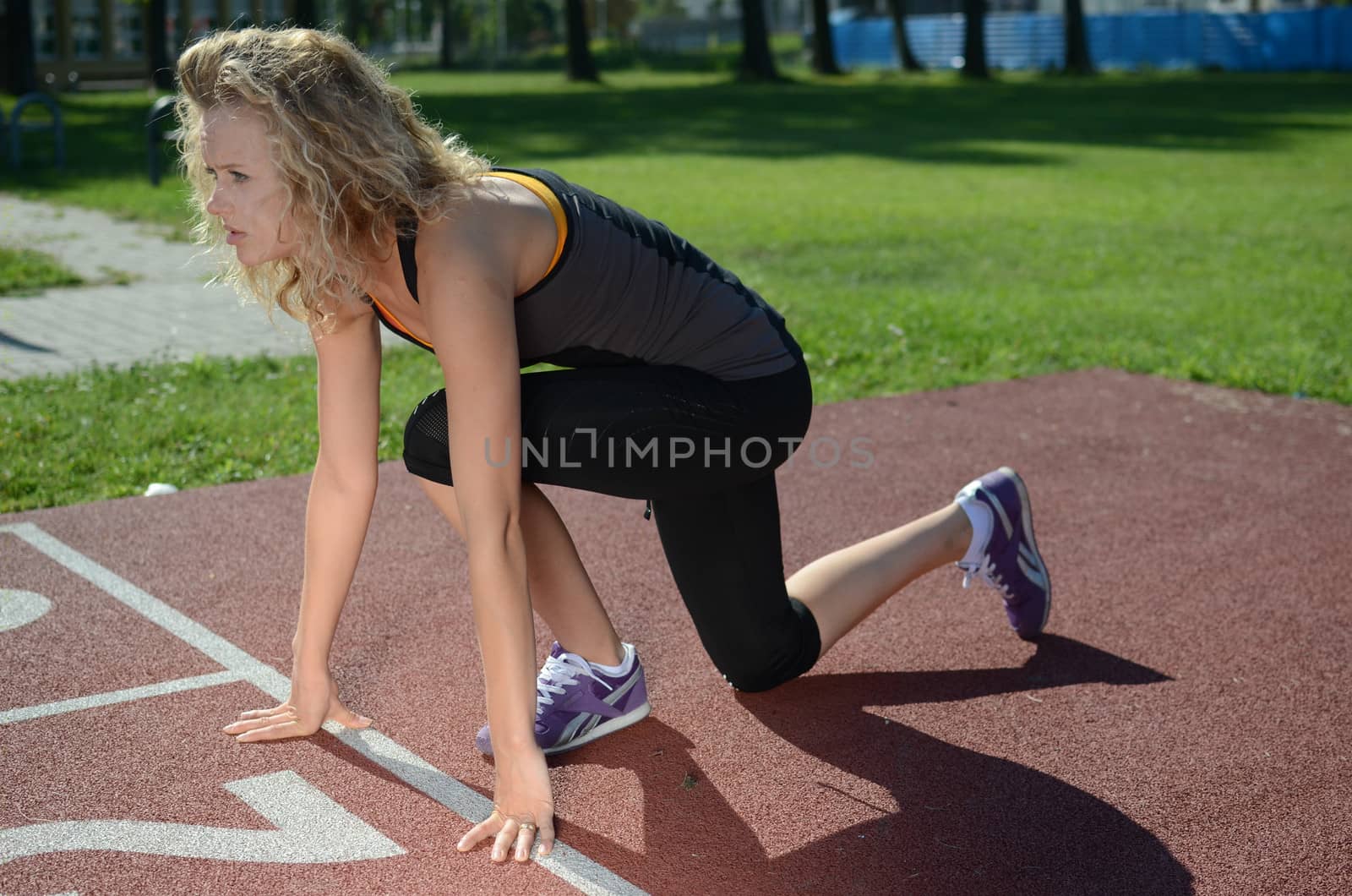 Young female runner prepares for the ran, sets her hands and feet. Blond girl, wearing sport's outfit.