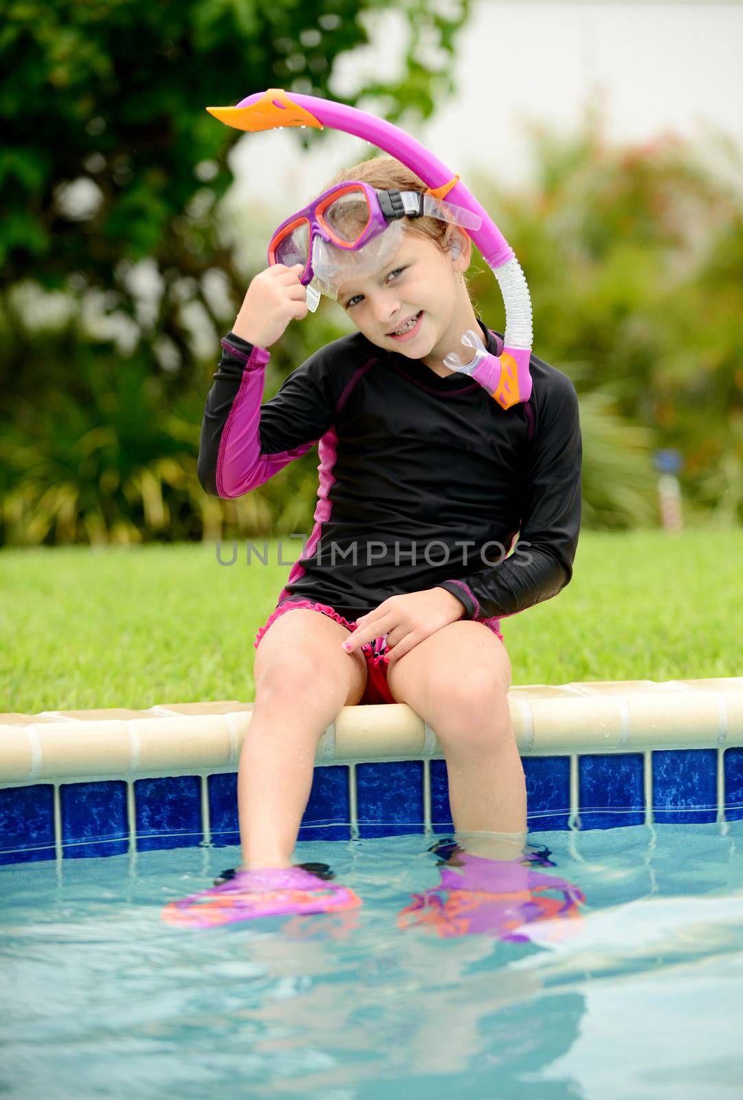smiling child sitting on edge of pool with swimming goggles and a snorkel