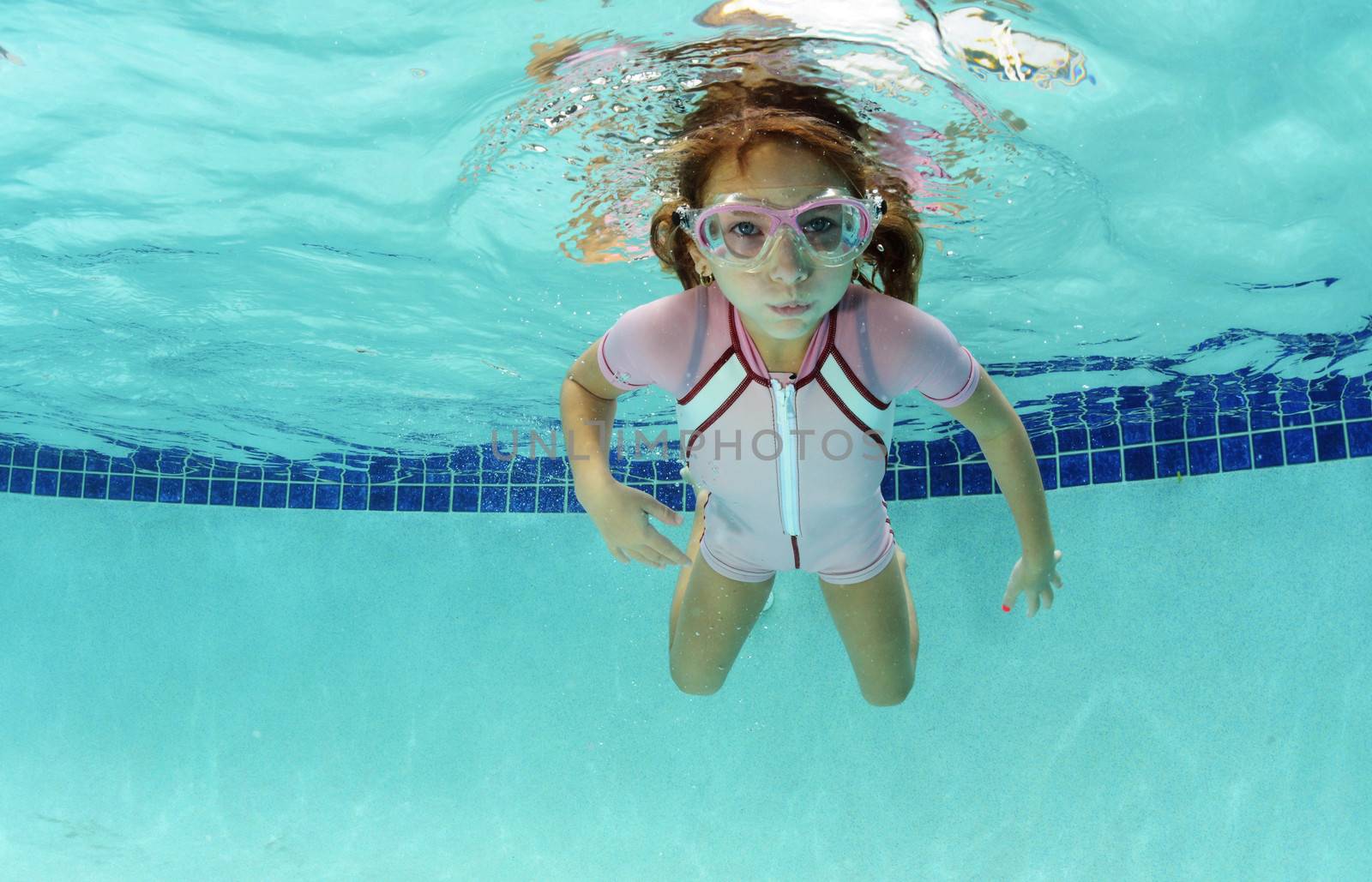 young girl holding breath underwater in swimming pool