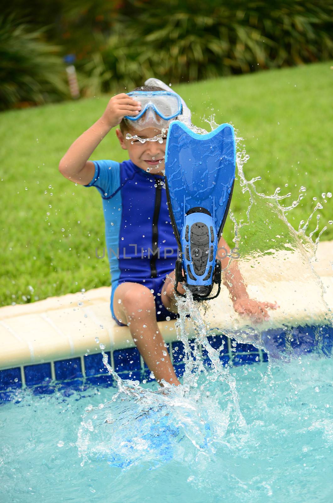 boy child splashing water with swimming flippers in summer on edge of pool