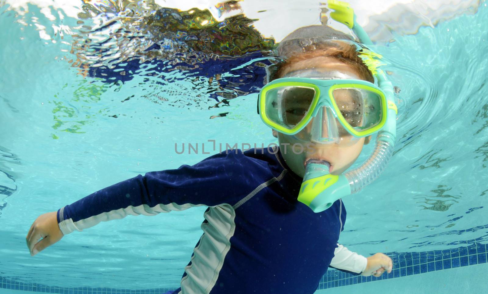 child snorkeling and swimming in pool with goggles