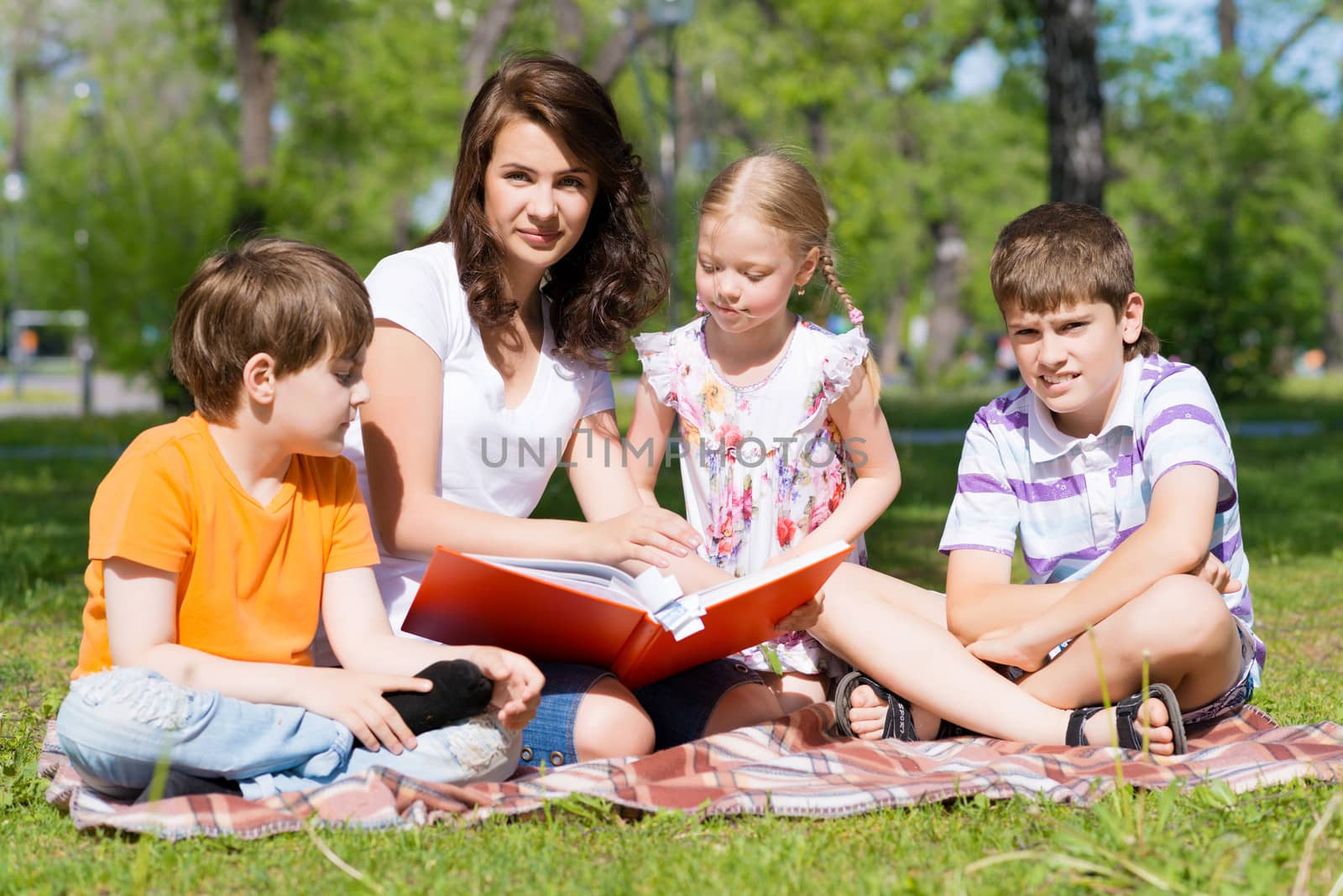 teacher reads a book to children in a summer park by adam121