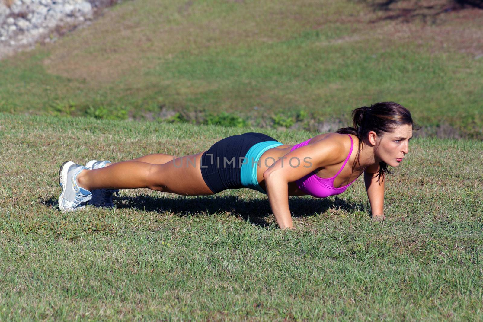 A lovely young athlete does pushups outdoors.  Generous copyspace.