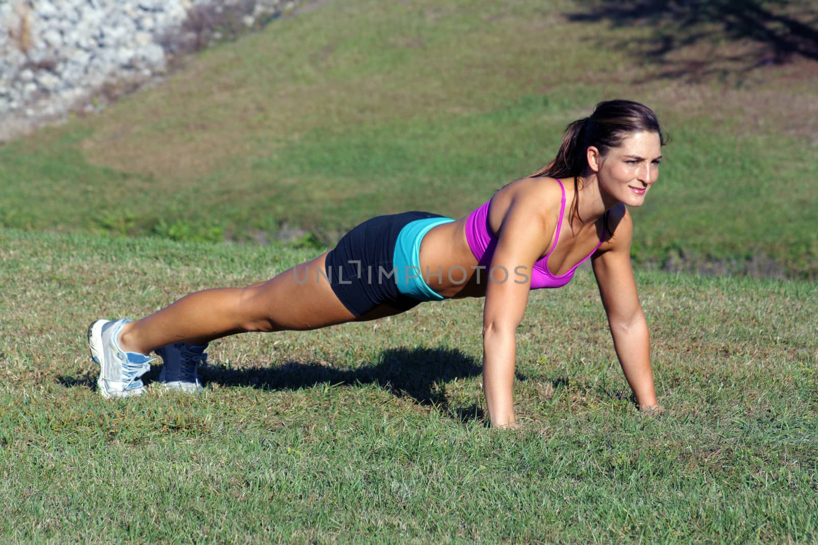 A lovely young athlete does pushups outdoors.  Generous copyspace.