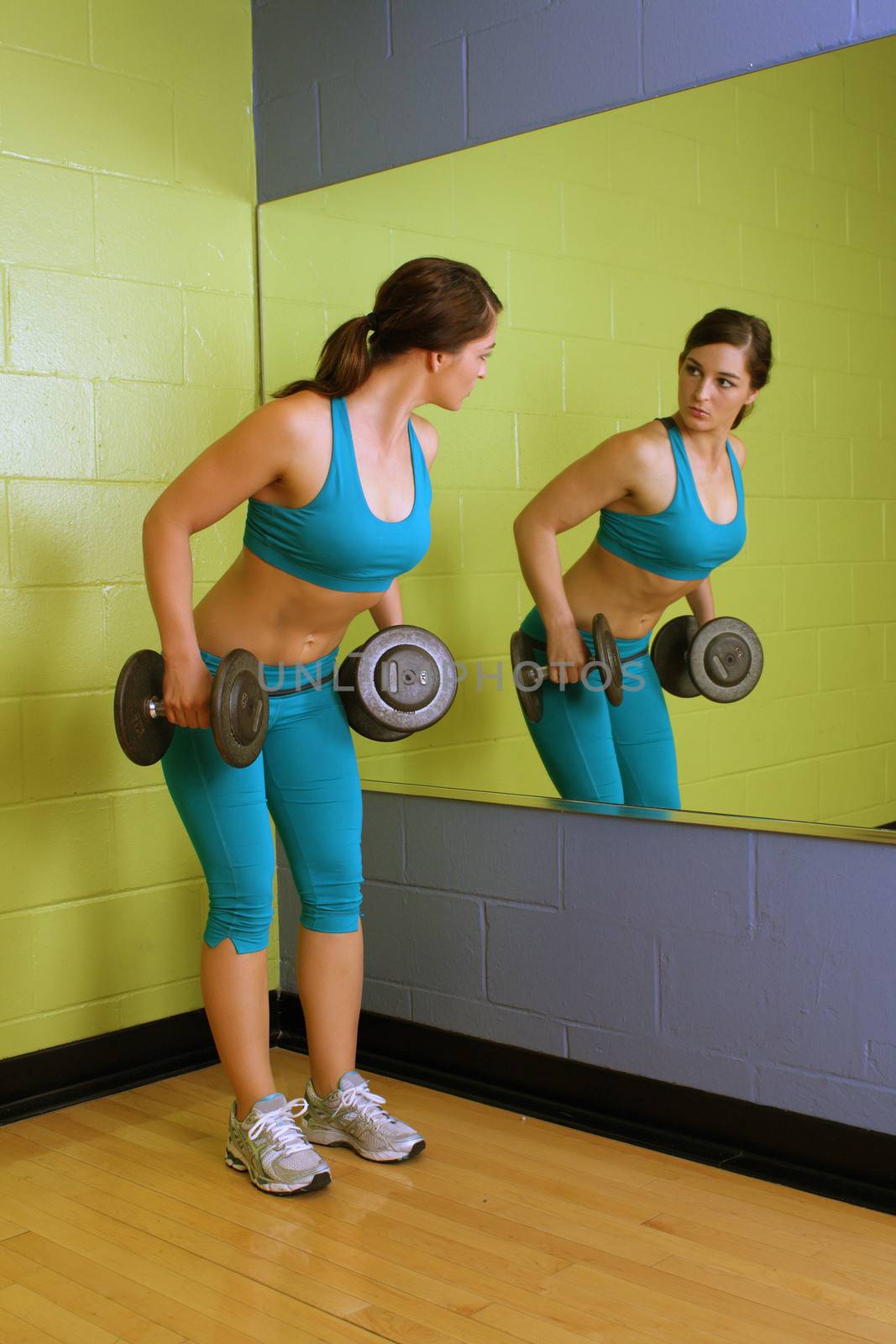 A lovely young brunette with exceptional muscle tone works out with hand weights in front of a mirror.