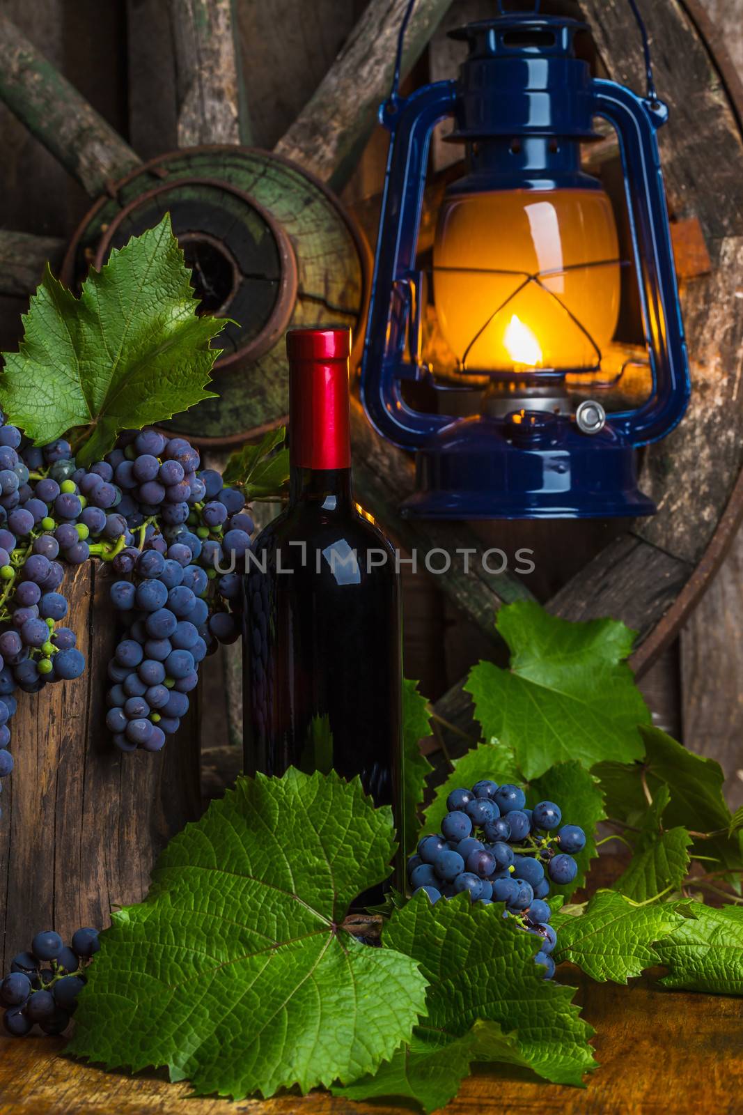 Bottle of red wine with grapes on a background of a kerosene lamp