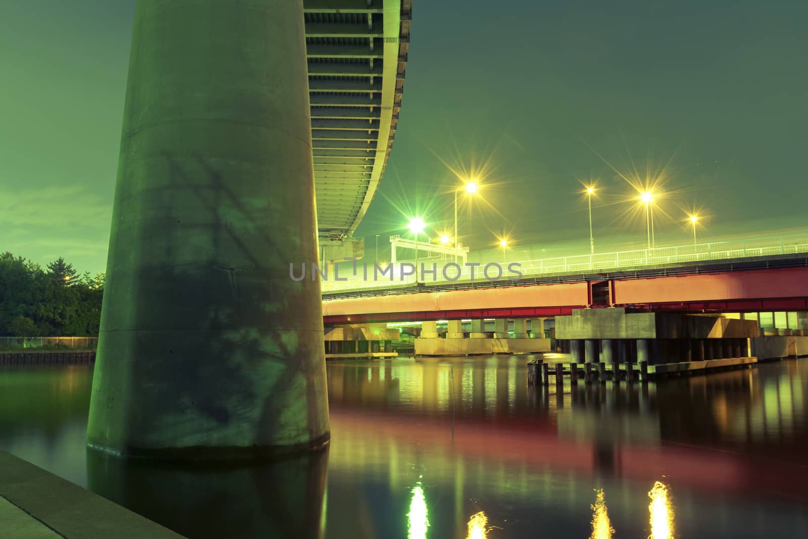 huge highway support on foreground with red bridge illuminated by night in Tokyo, Japan
