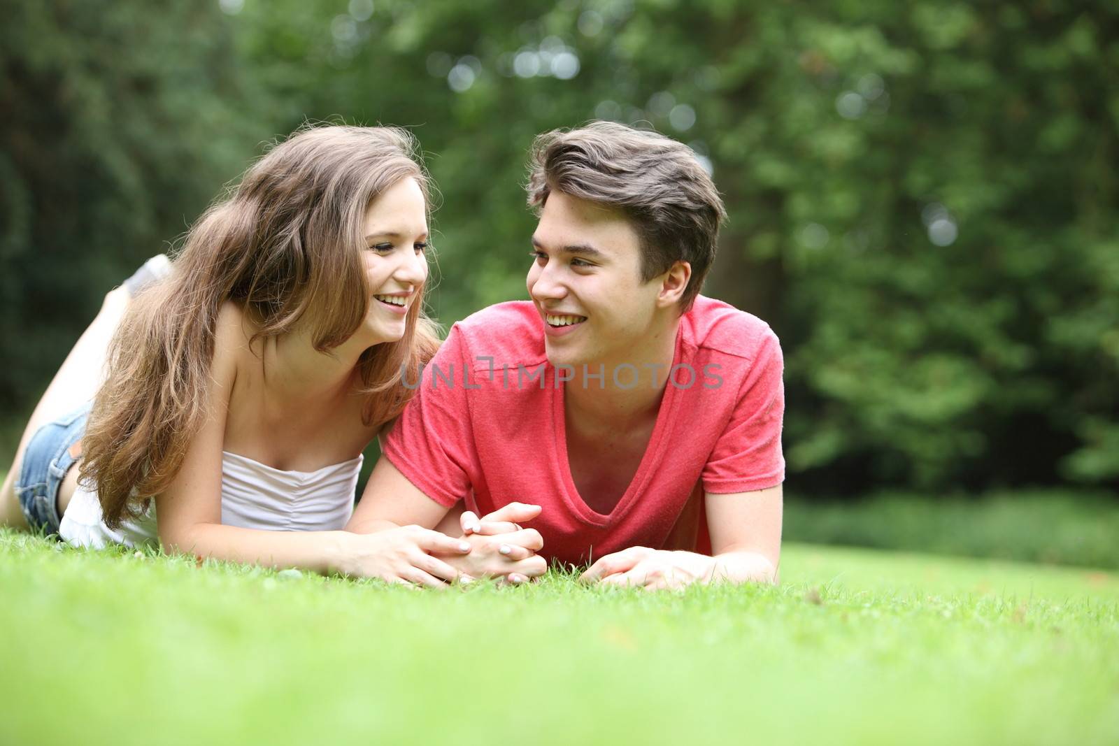 Teenage boy and girl lying on the grass holding hands and smiling at each other as they relax in the sunshine