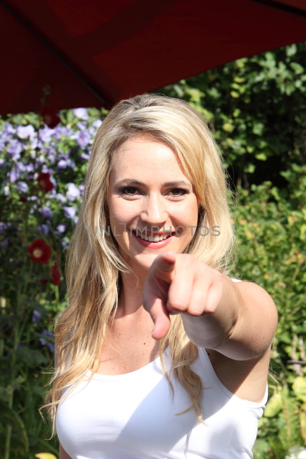 Beautiful woman standing in the garden in the sunshine pointing at the camera with a playful smile