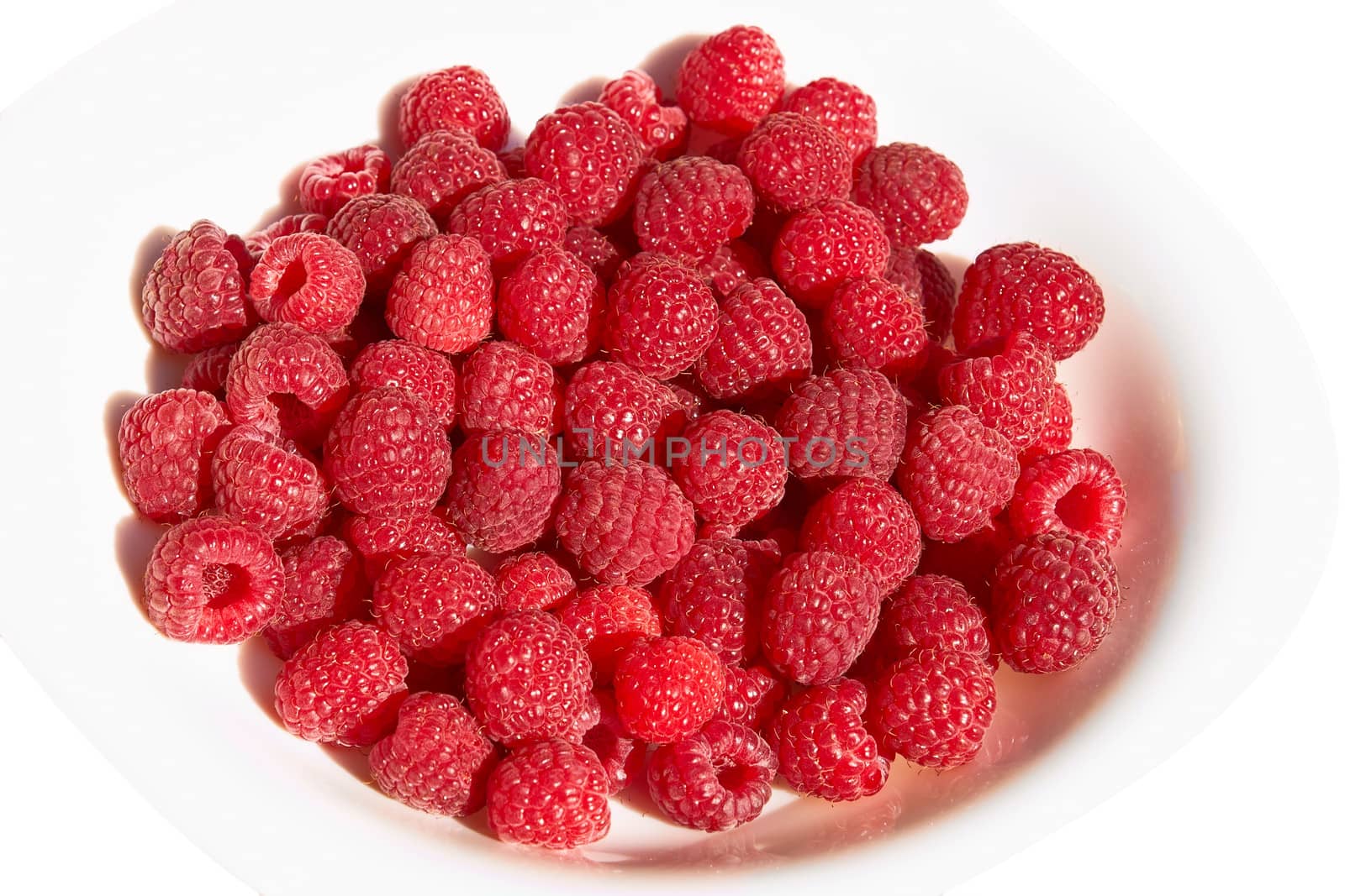 Lots of ripe red raspberry berries on a plate over white background close up