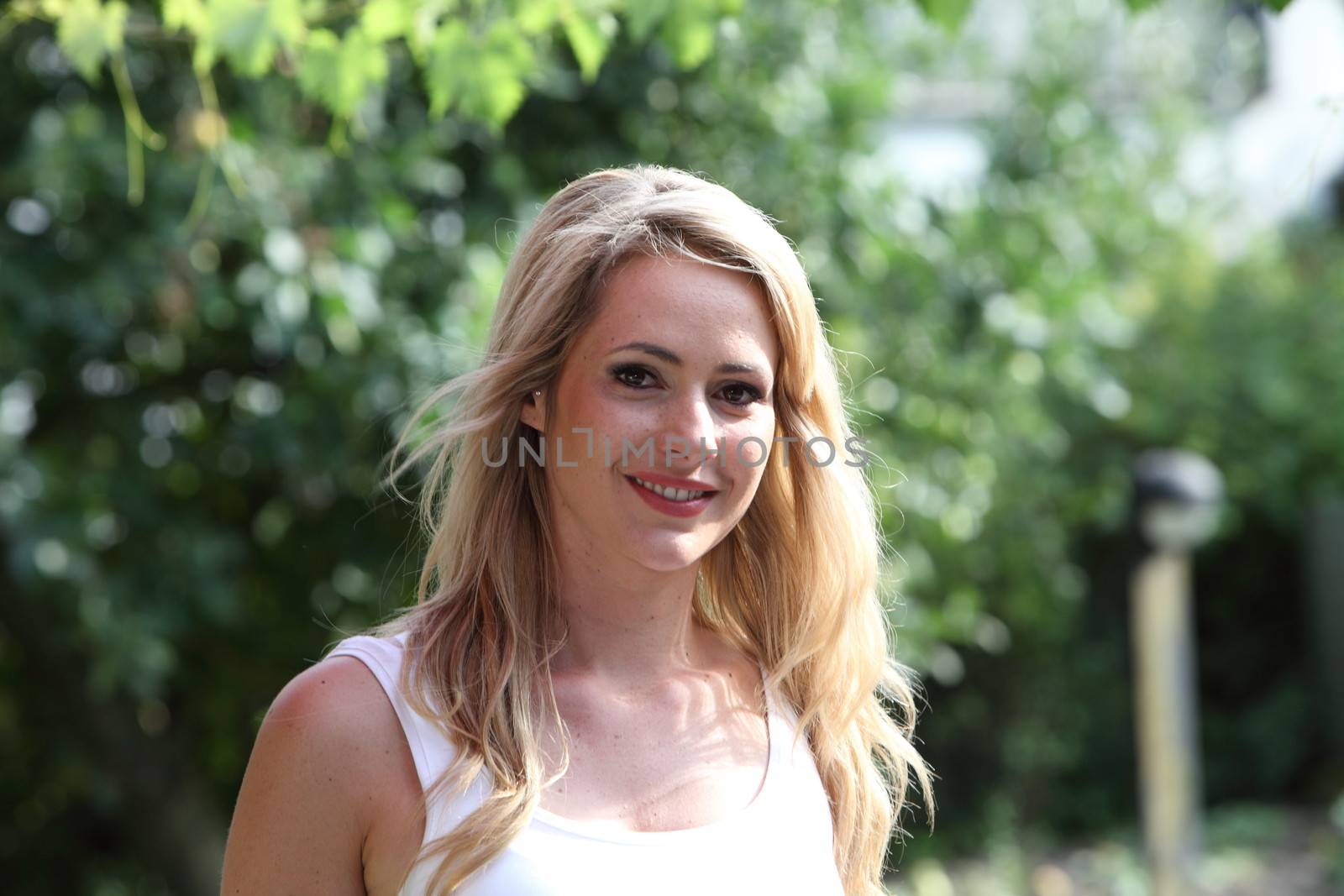 Attractive blond woman in the garden standing looking at the camera with a smile as she enjoys the summer sunshine