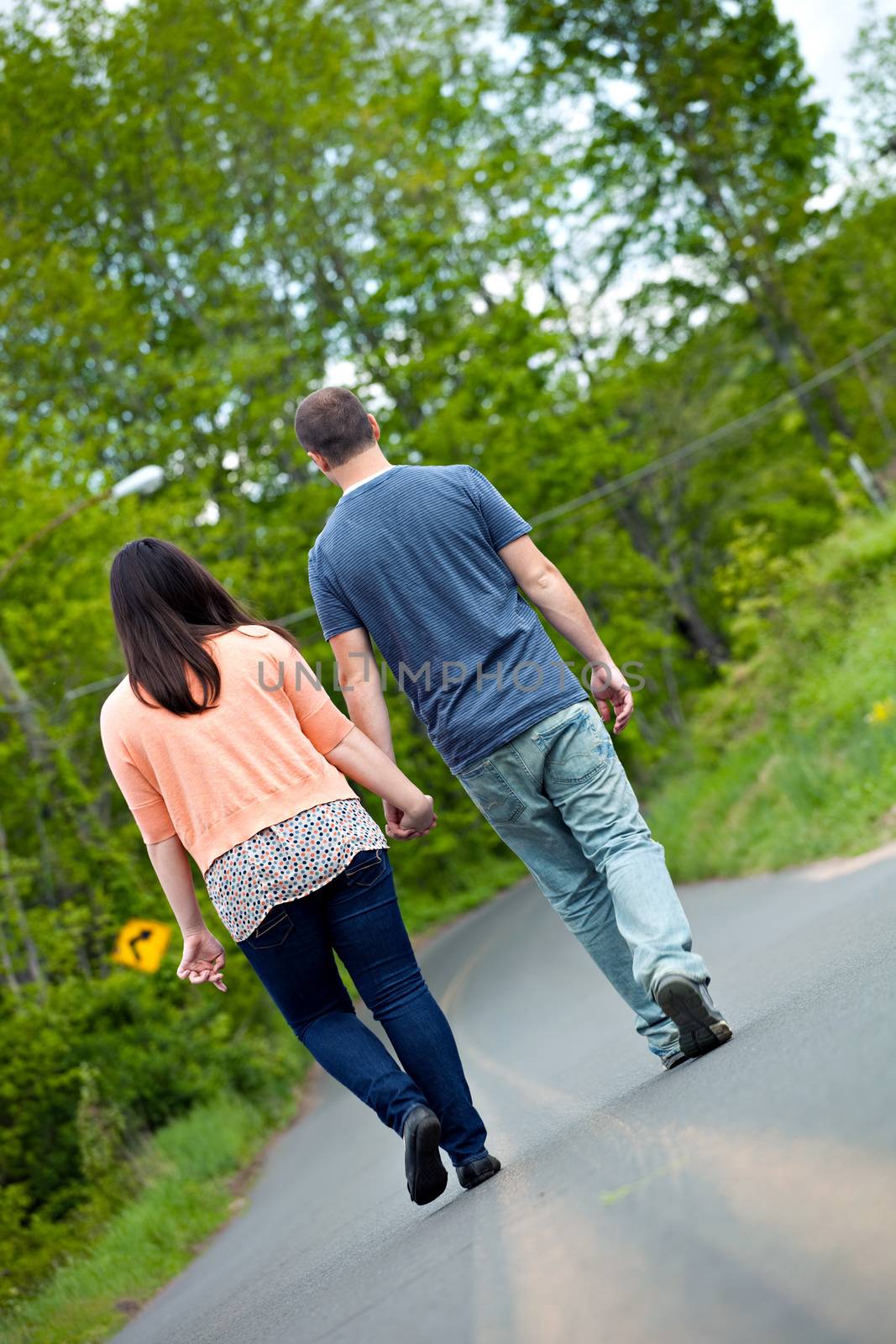 Young happy couple enjoying each others company outdoors walking down an empty road. A very fitting theme for the start of marriage or any romantic relationship.