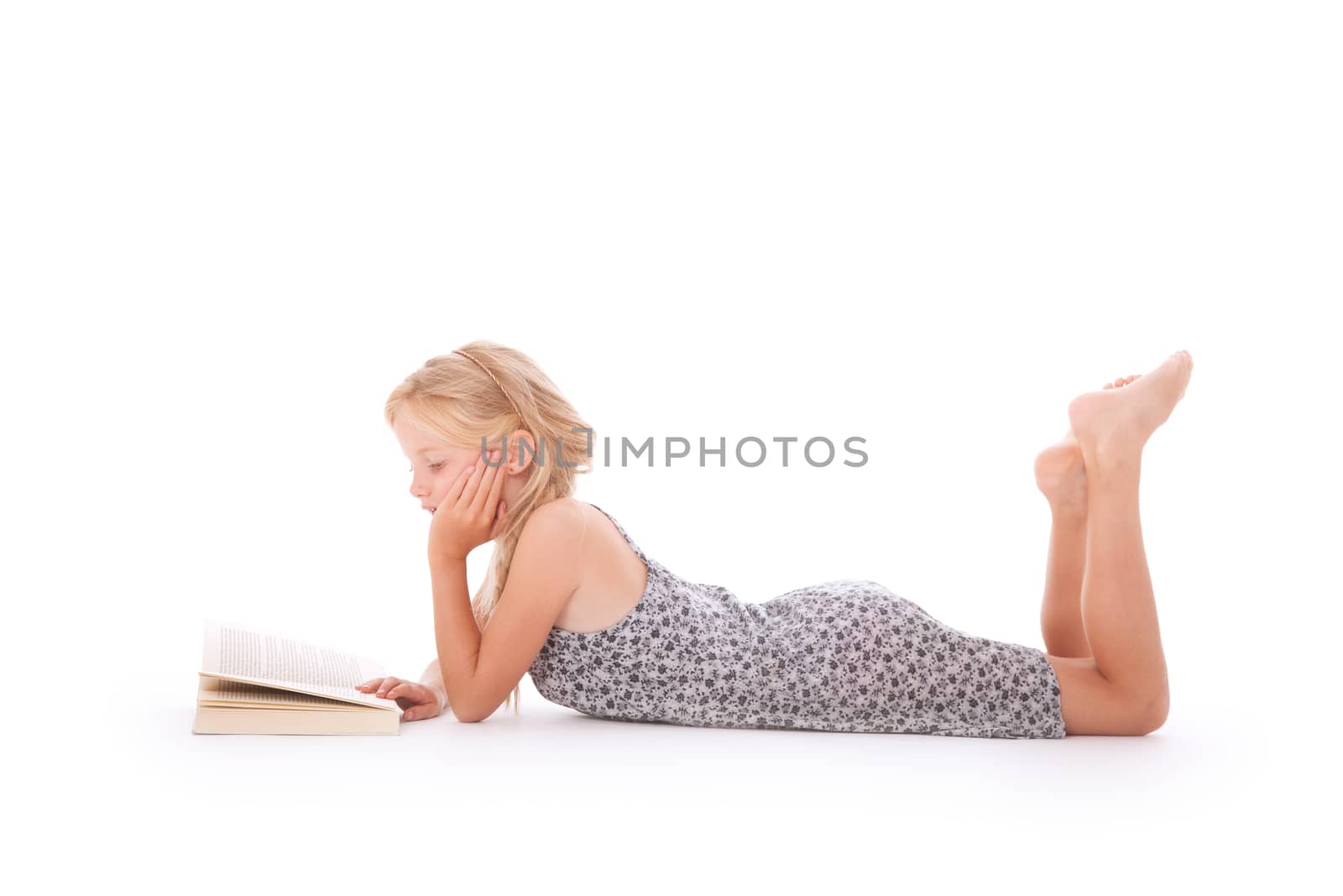 young girl reads a book lying down on the floor of studio against white background