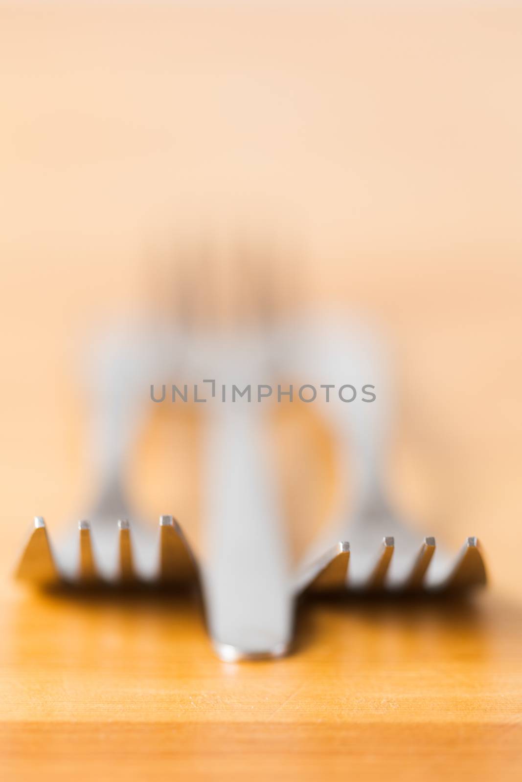 Silver cutlery abstract with very shallow dof to the tips of the forks as they lie on a wooden counter facing the viewer