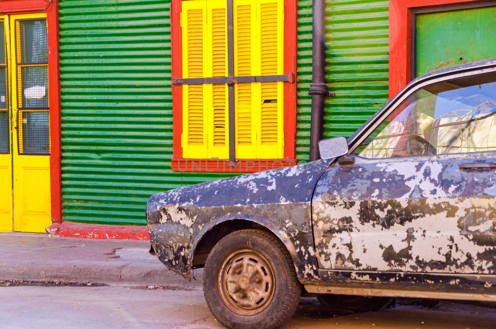 Old damaged car in front of a brightly colored building in La Boca neighborhood of Buenos Aires