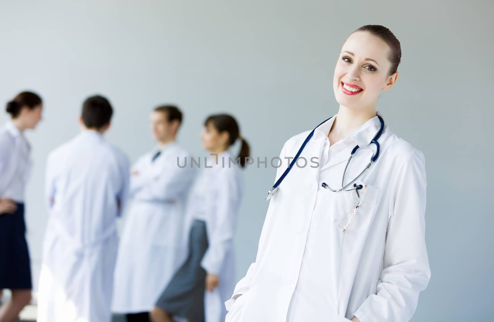 Attractive female doctor in white uniform with colleagues at background