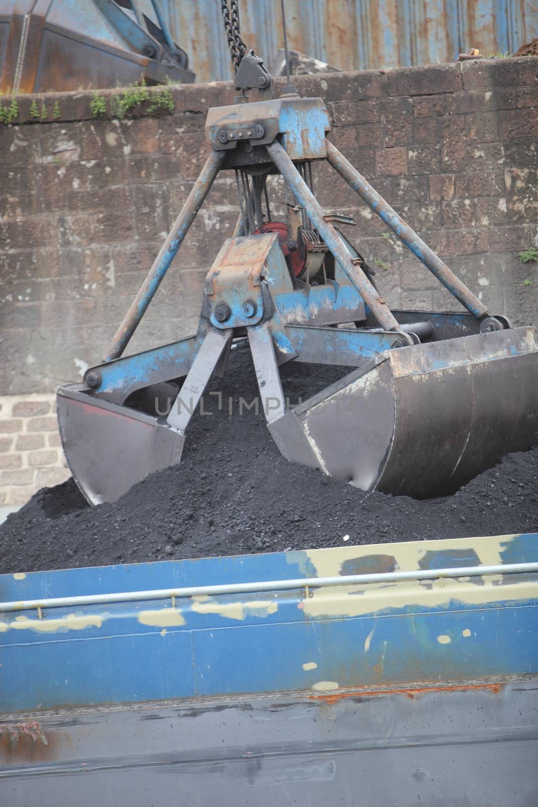 Mechanical bucket on a crane picking up a load of crushed stone from a quarry or mine that has been transported in a metal container