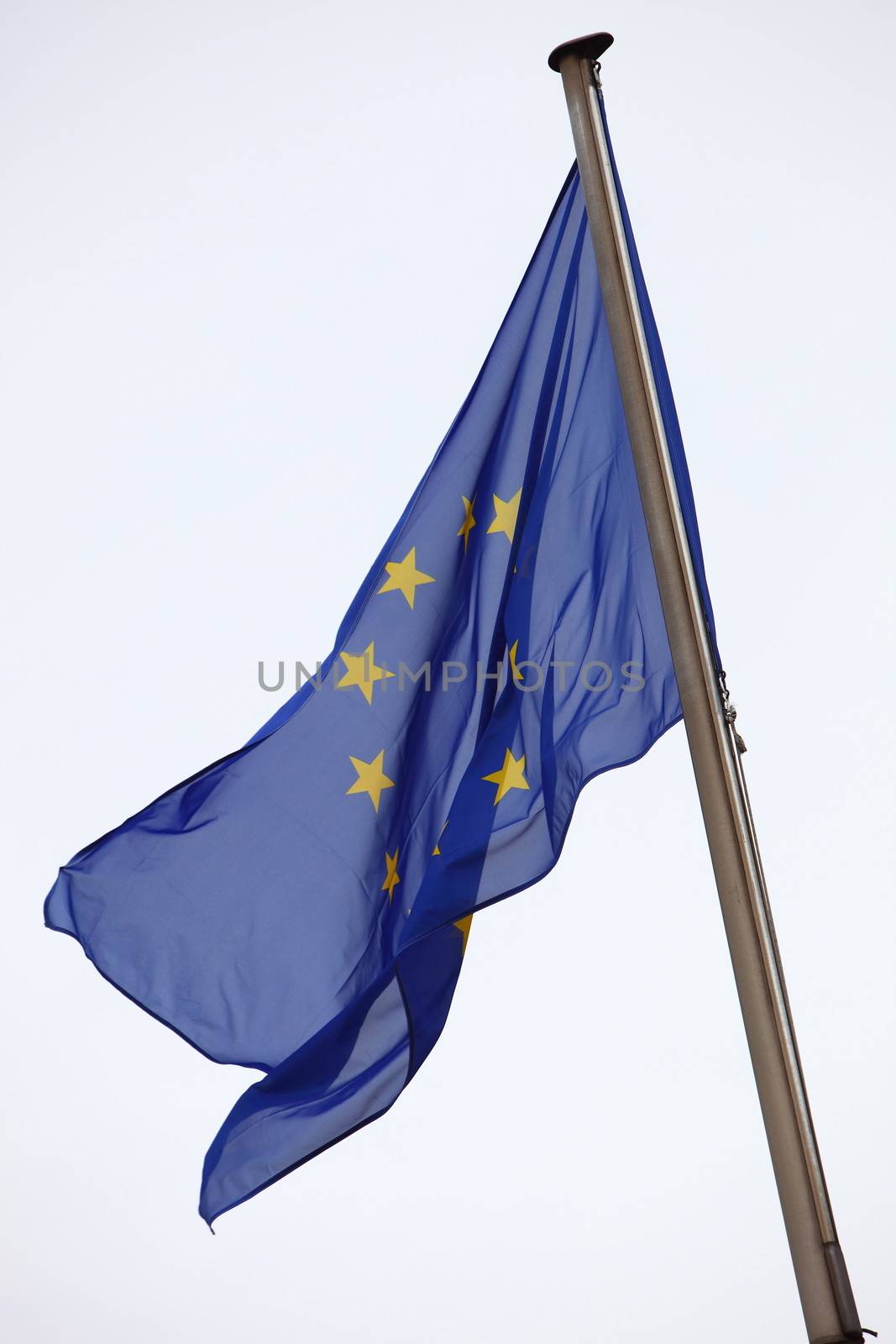 European Union flag flying on a flagpole against a light grey sky with copyspace