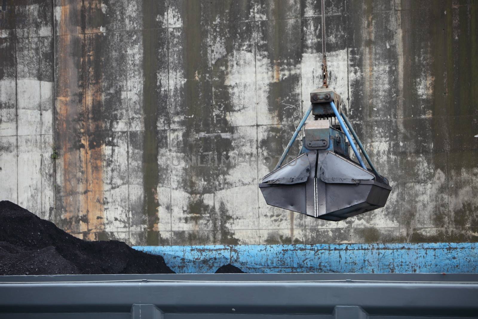 Bucket suspended from a crane hanging over a metal bin at an industrial site with copyspace