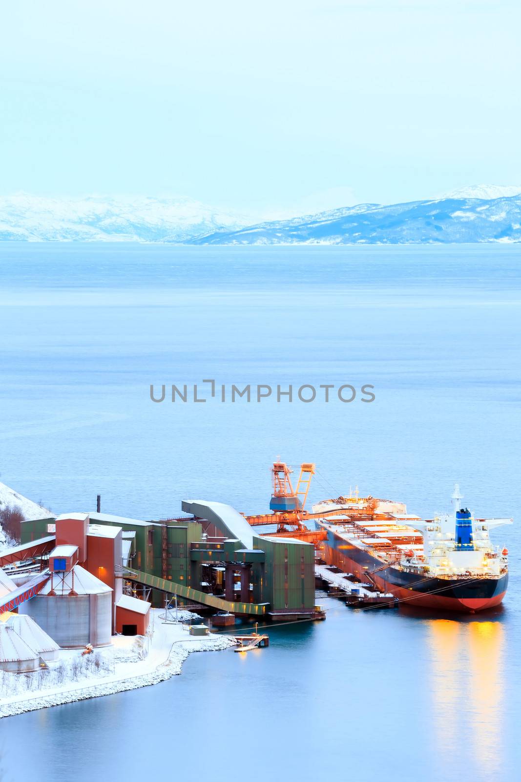 Industrial Container Cargo freight ship with working crane bridge in shipyard at Iron Ore Mine Factory Plant in Narvik Norway