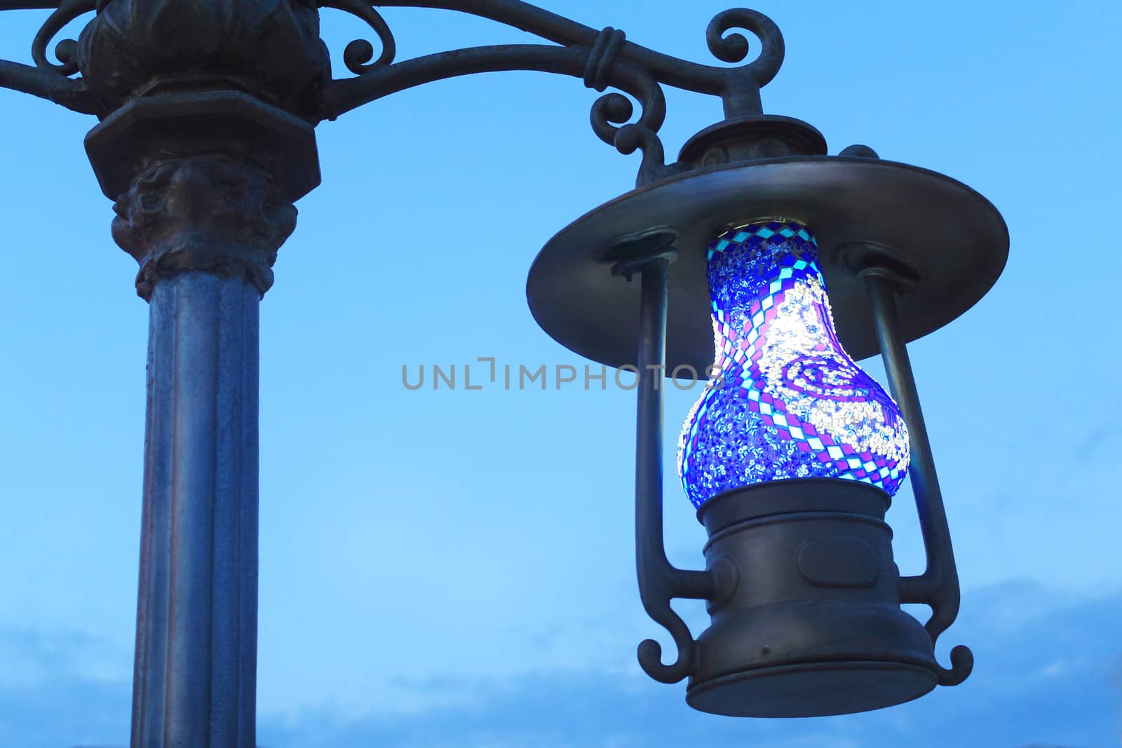 Lamp on a pole on the street, made in the form of antique lamp. Photographed on the background of blue sky.
