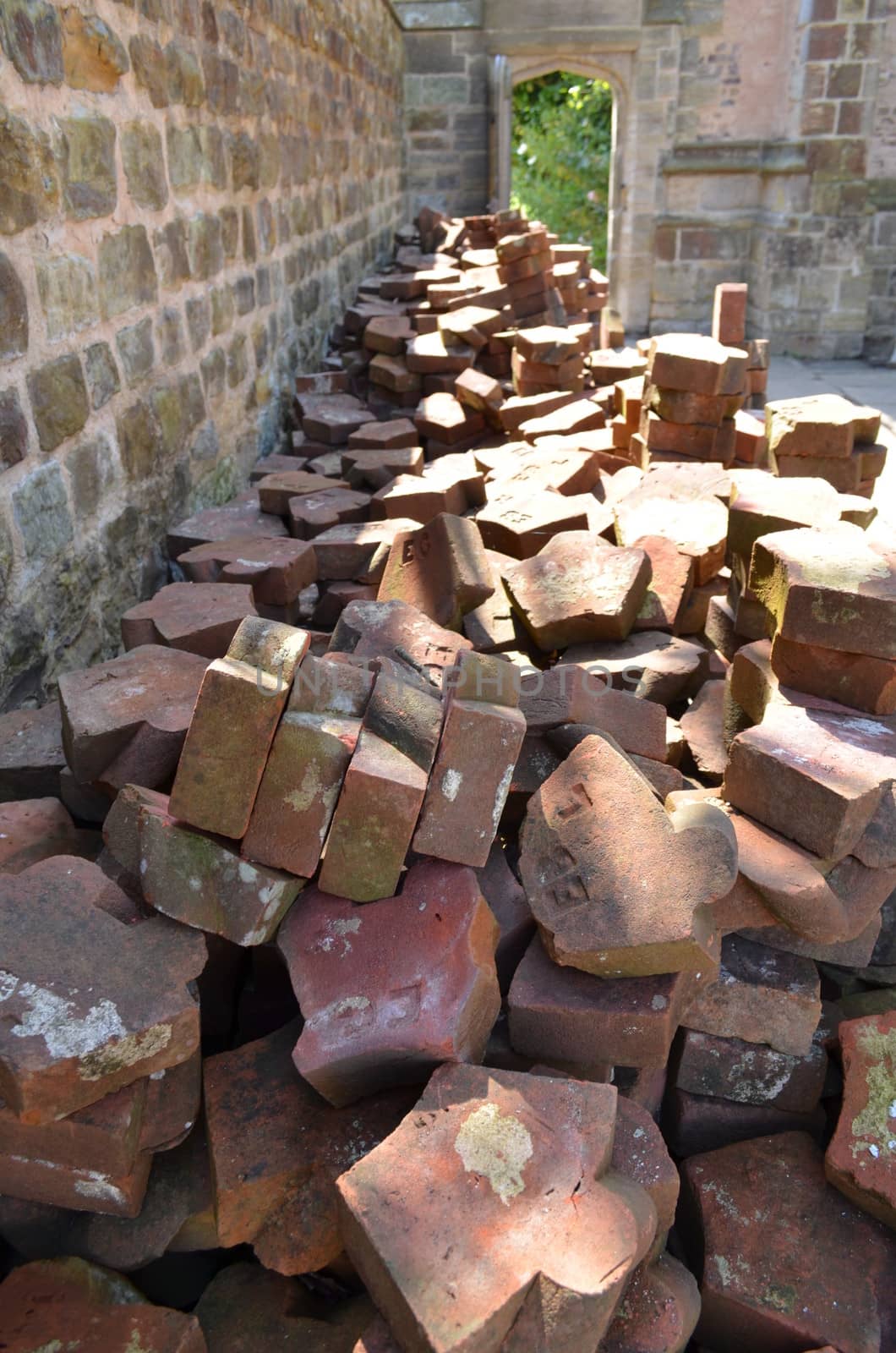 Pile of old clay bricks and roof tiles left in a garden.