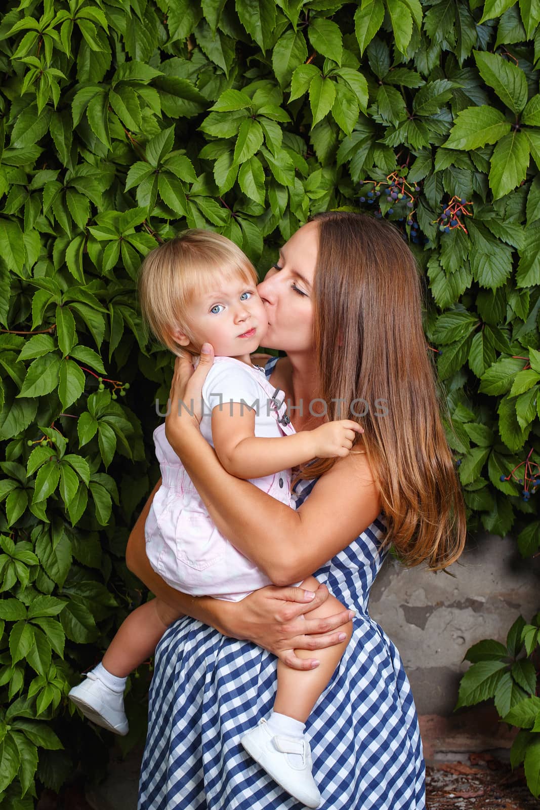 Mother holds daughter in his arms and kisses her on the cheek