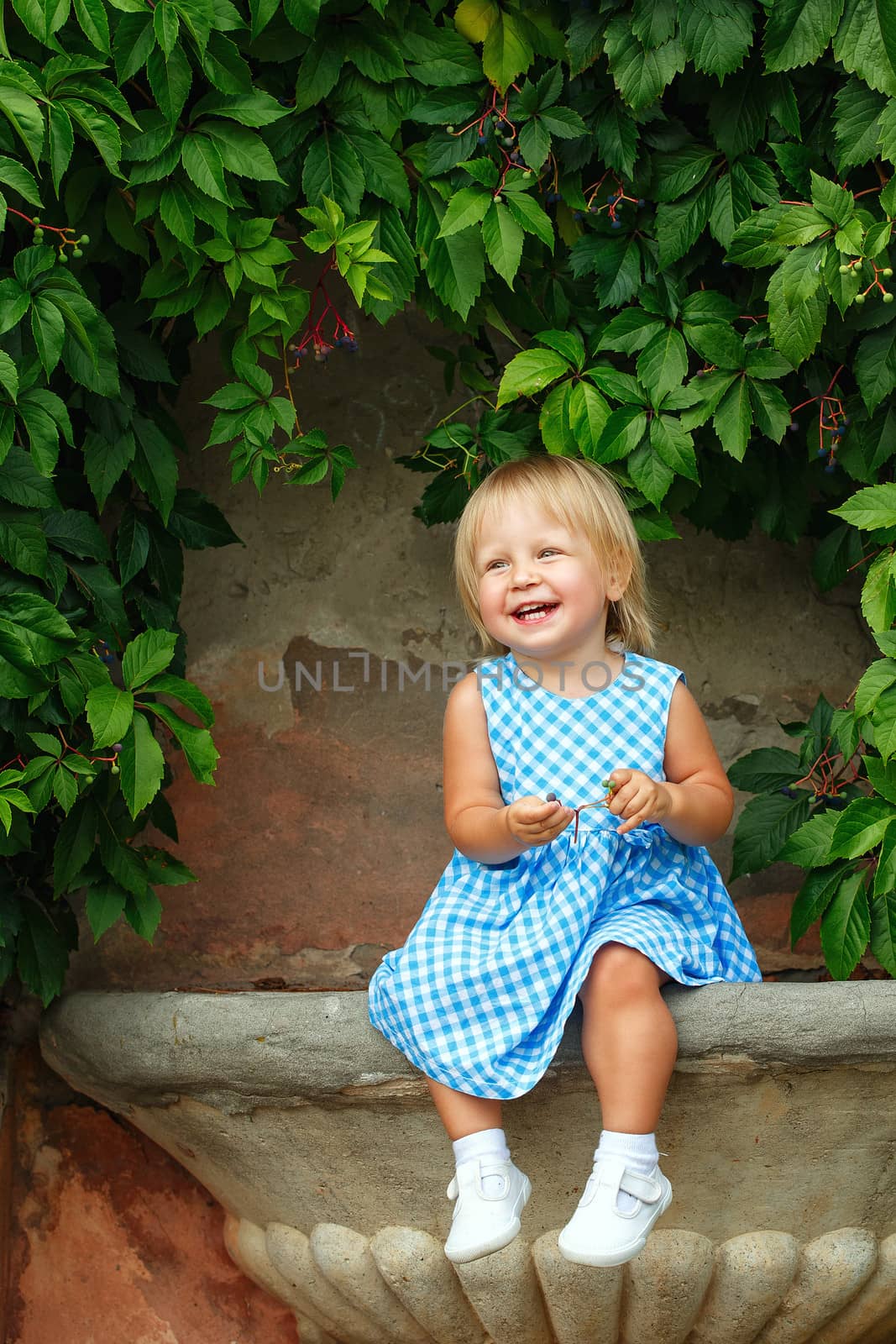 Little blonde girl on a background of green grape leaves