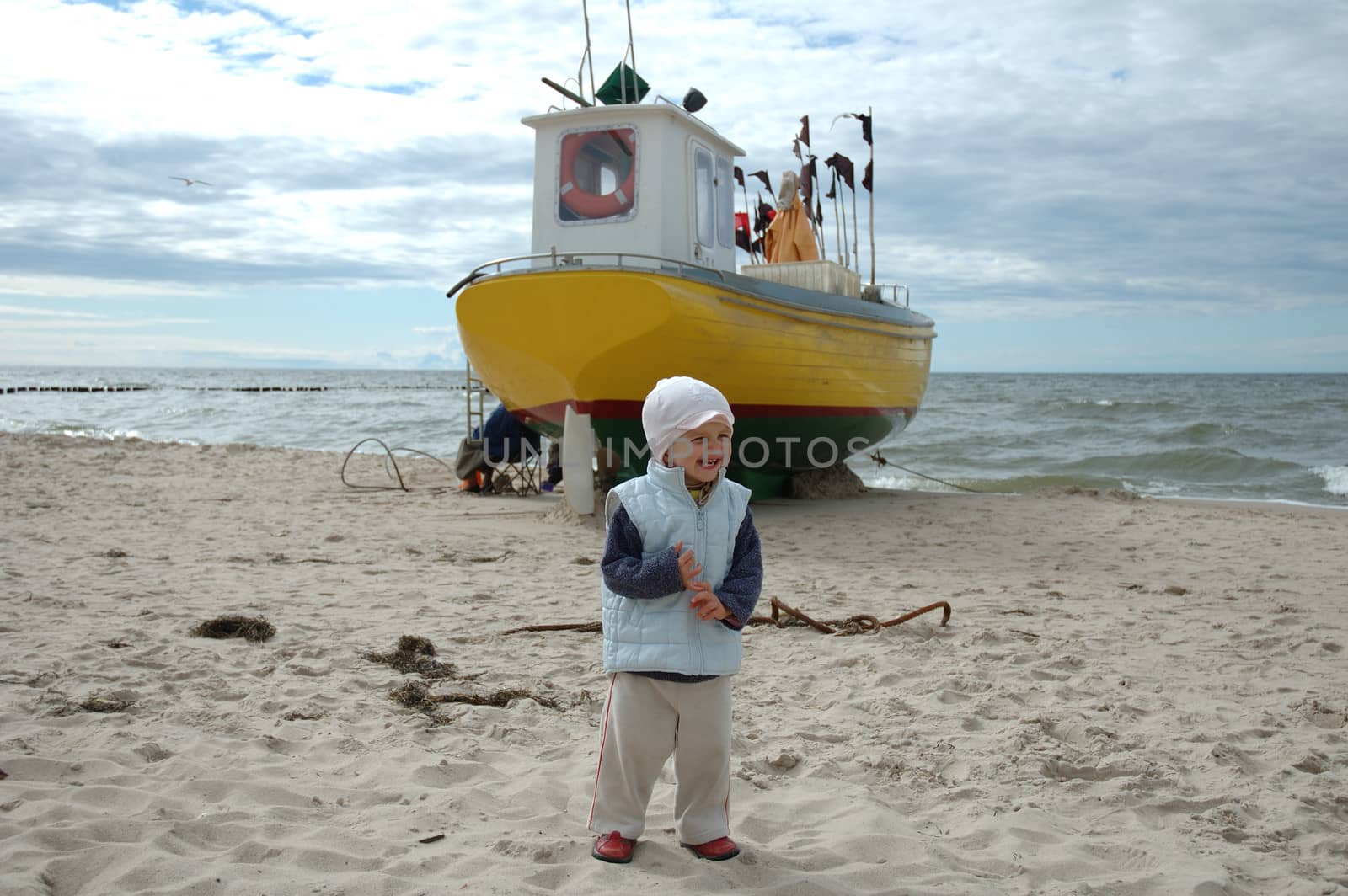 Little girl and fishing boat on beach somewhere in Poland