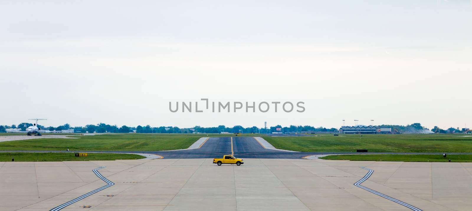 A yellow servicing truck moving on the middle of airport runway
