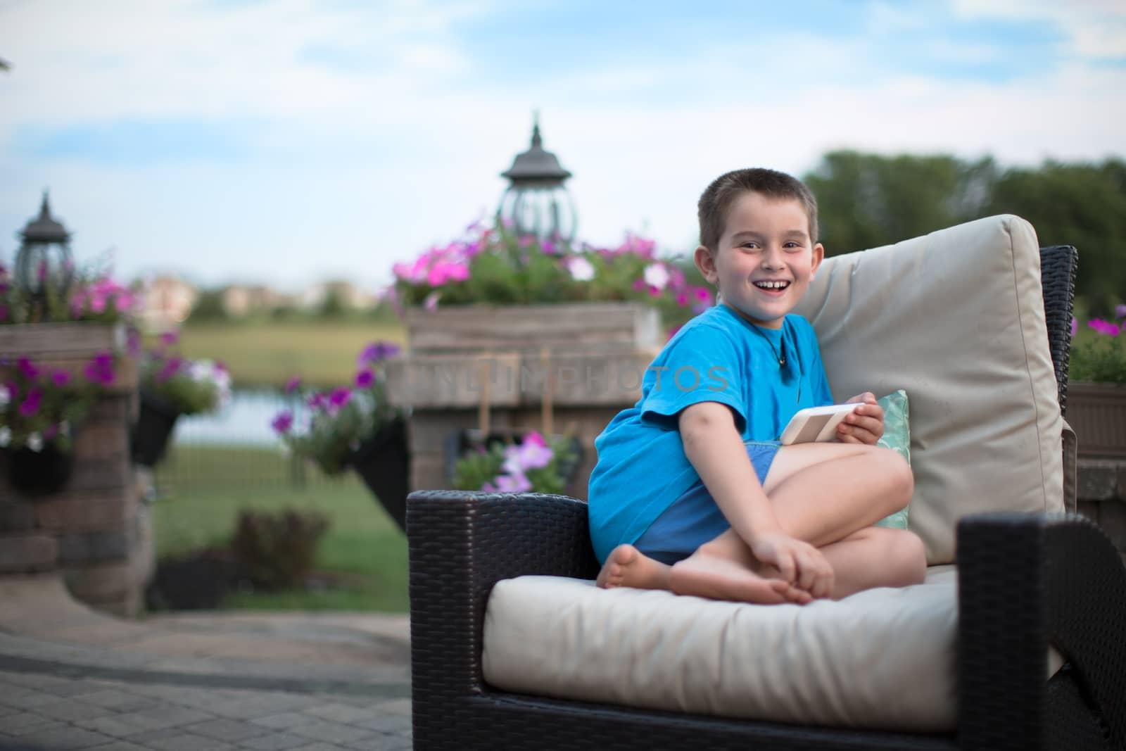 Young boy smiling at camera with a large genuine smile on the wicker seat at the patio