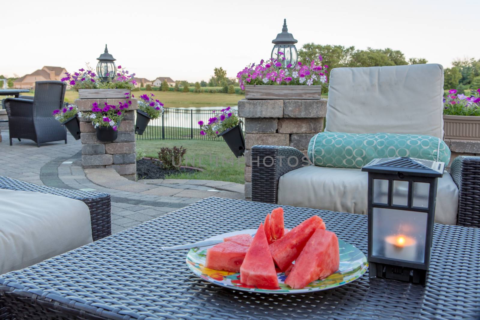 Brick patio and pillars with flower planters on the pillars. Looking  to the lake and watermelon on the table along with fly