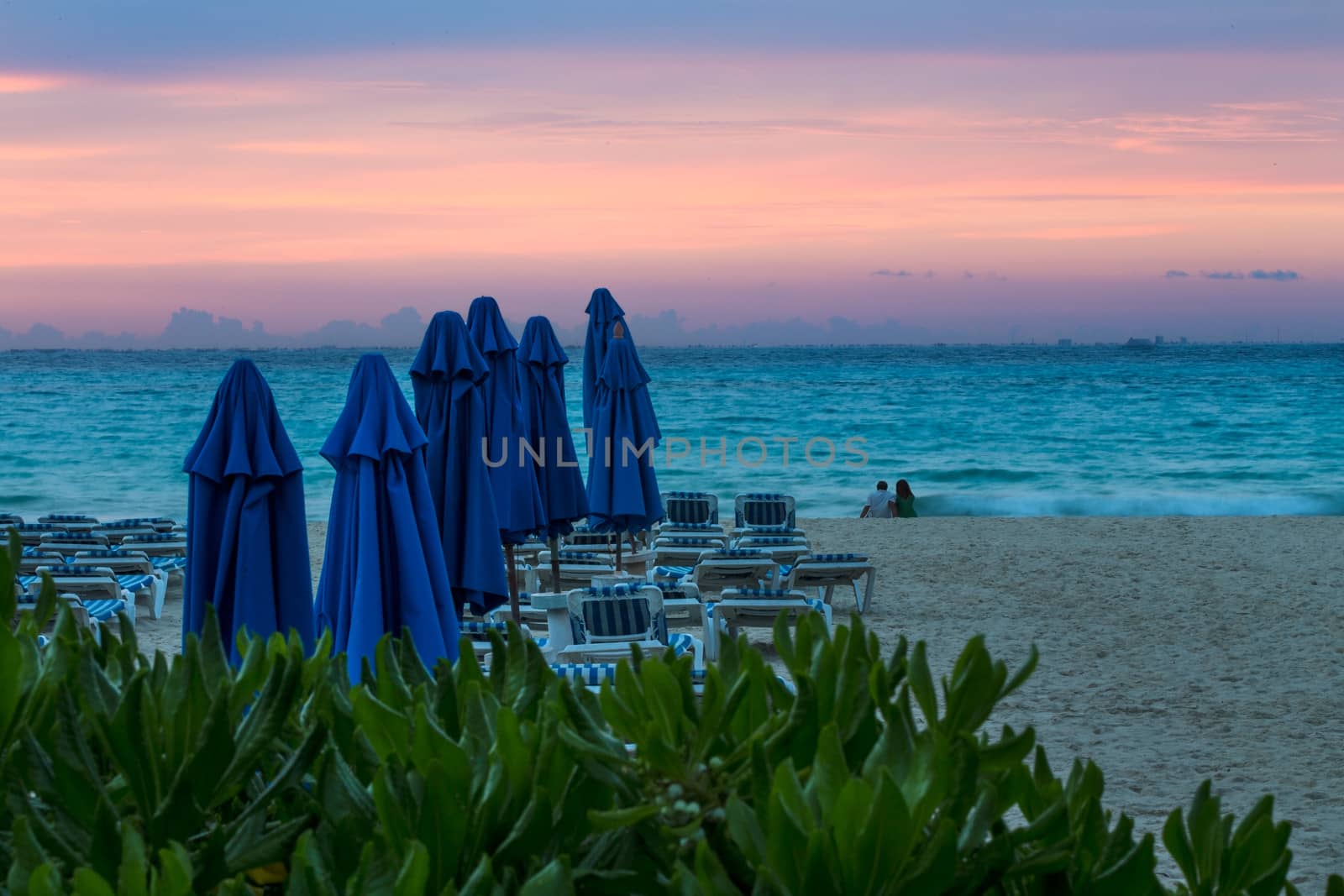 Couple sitting on the sandy beach looking at Cozumel Island at sunrise in Mexico