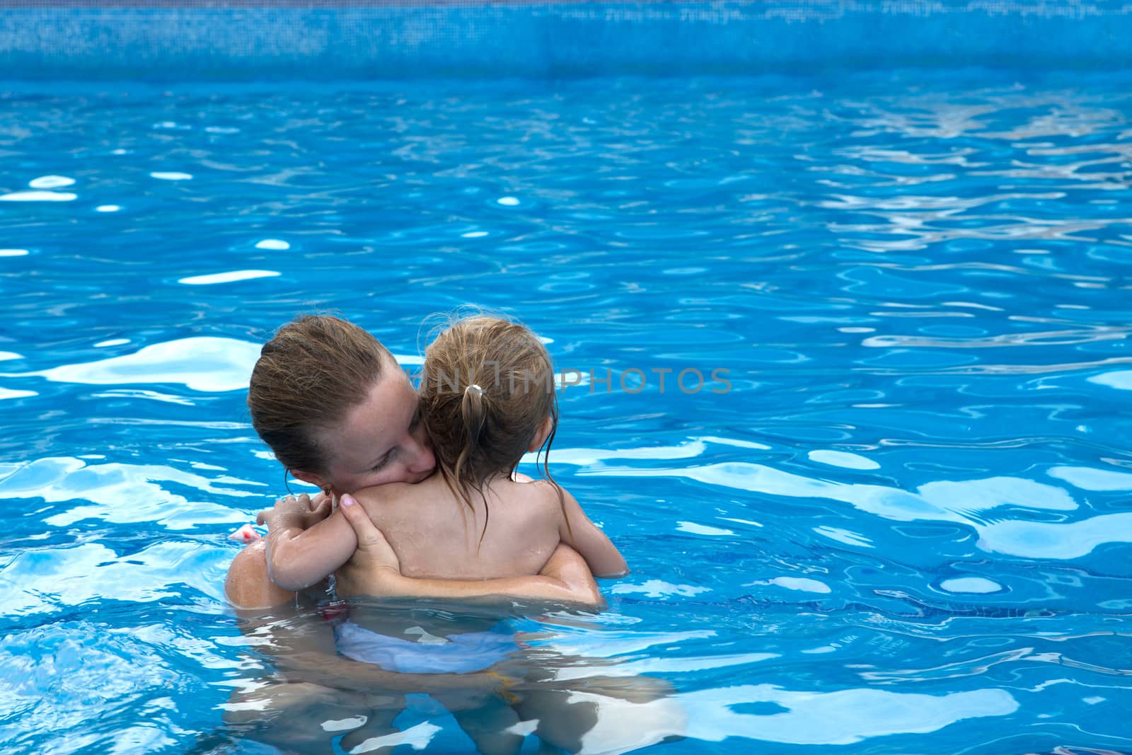 Mother and daughter cuddling in the pool with copy space on the right