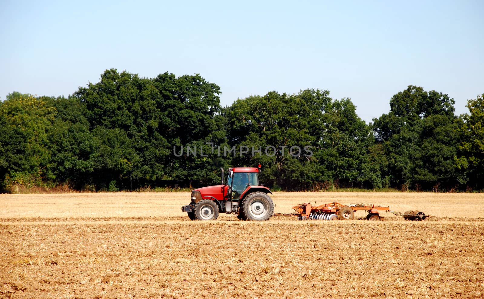 Red tractor and disc harrow breaking up the soil after harvest in a farm field - Kent, England