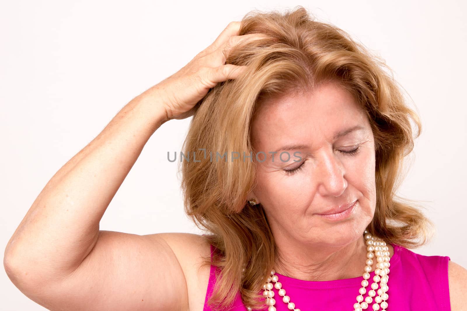 Attractive middle aged woman with a headache clutching her hand to the top of her head with downcast eyes and a serious pained expression, isolated on white