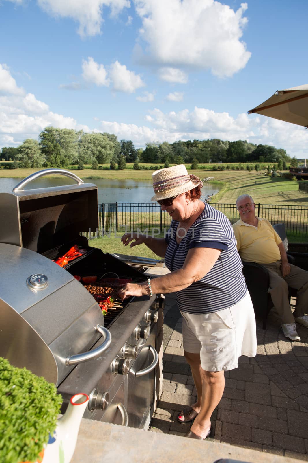 An old couple happily grilling some barbecue near a lake.