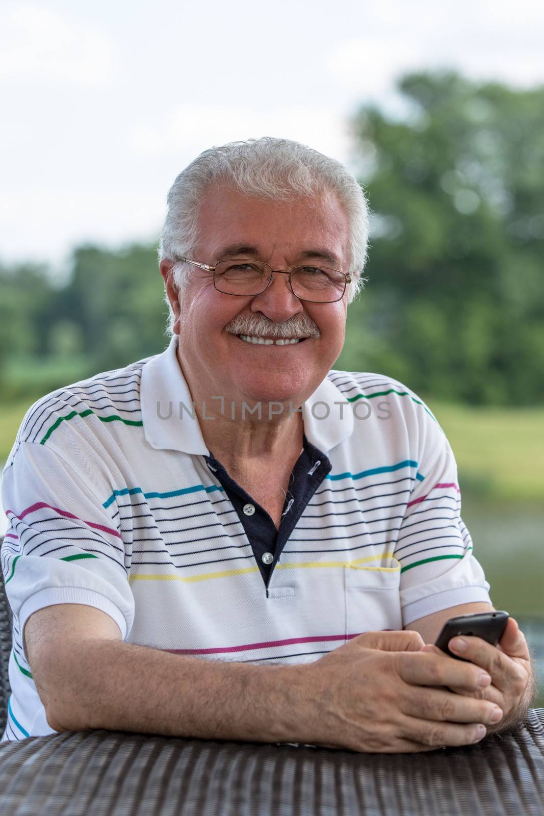 Grey hair senior gentleman looking trustfully with his glasses while holding his phone.