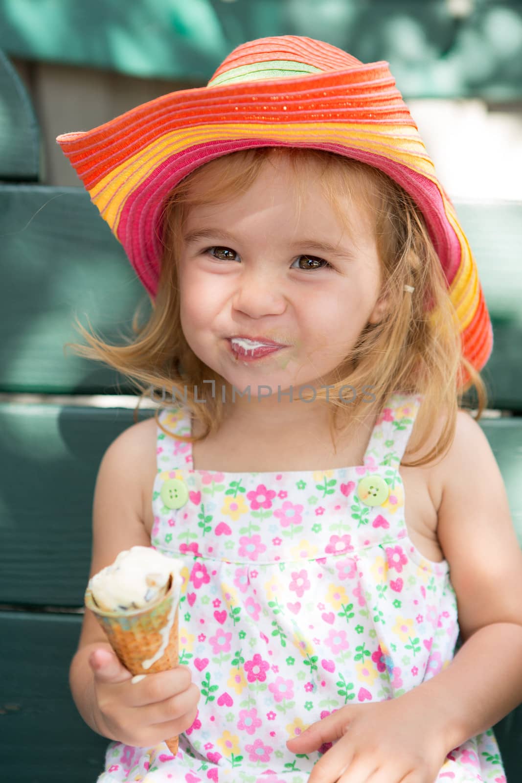 Sweet little blond girl in a straw hat eating her ice cream in the summer sunshine