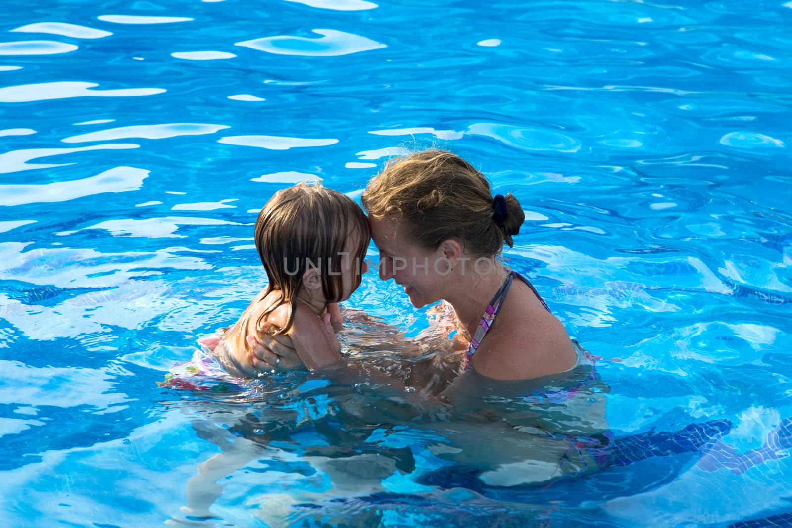 Mother and doughter head to head having passionate great time in the swimming pool.