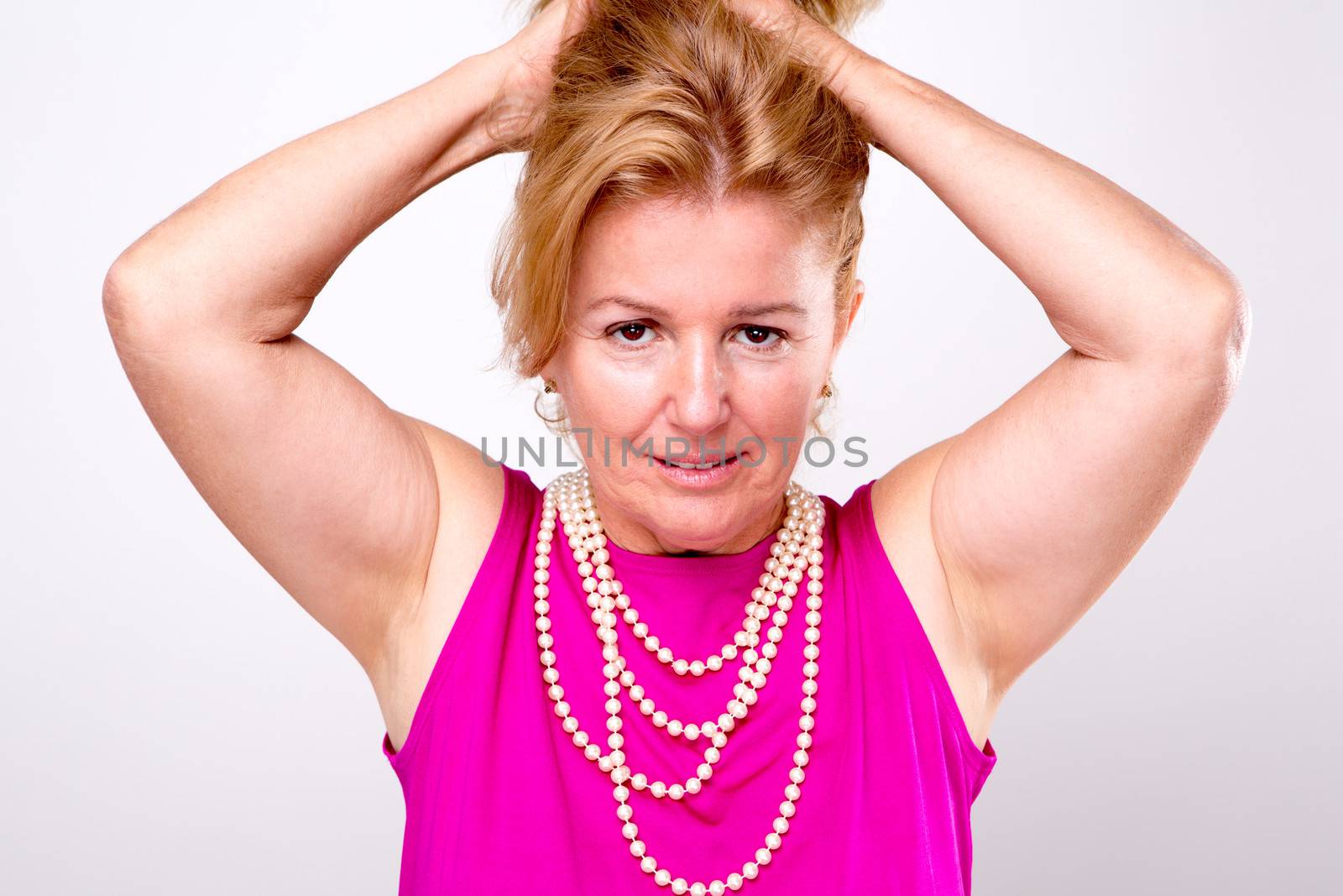 Mature Blonde Lady with Both Arms up holding her hair, she has pearl necklace and  pink shirt