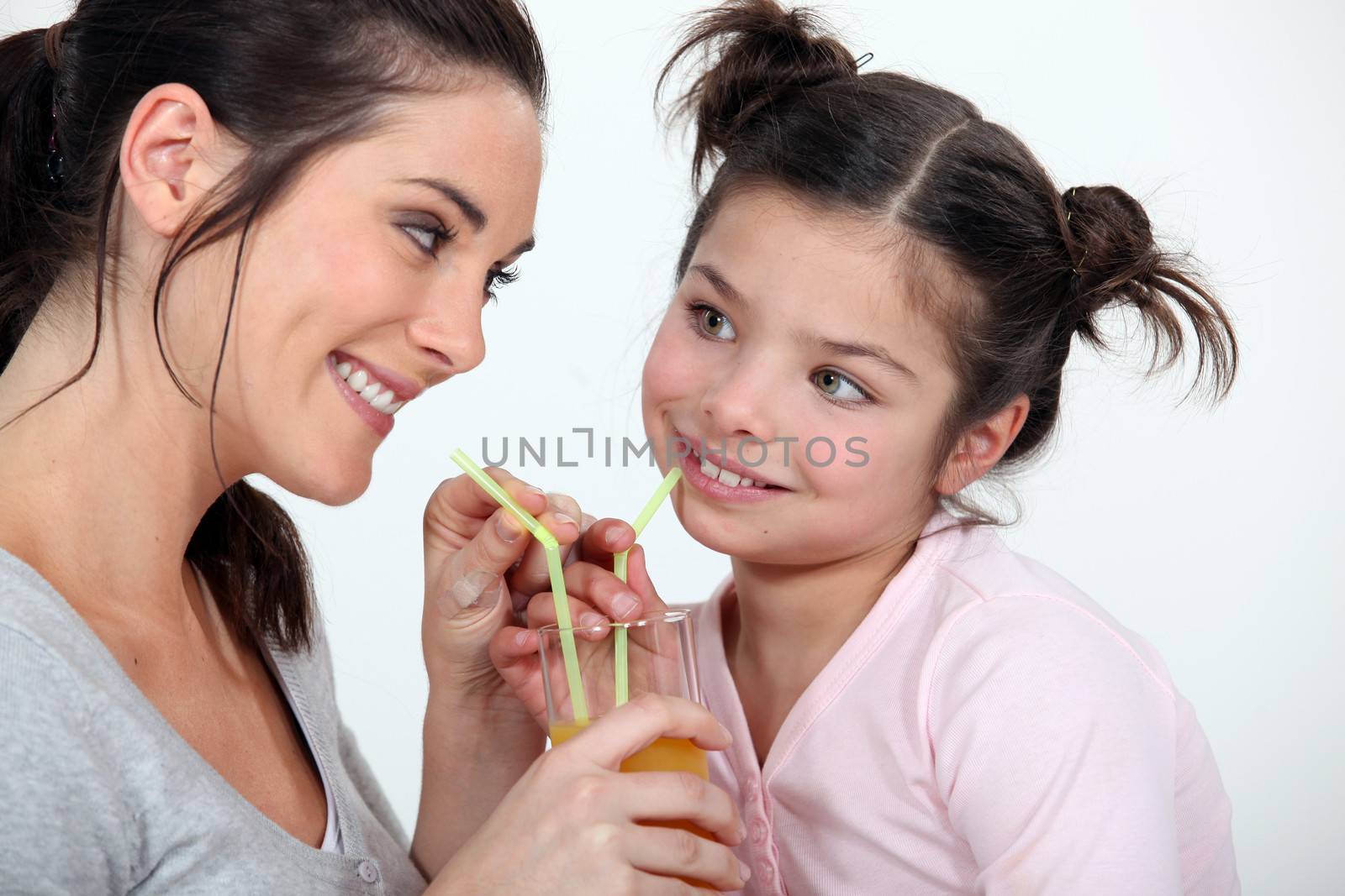 Woman sharing a glass of juice with her little sister by phovoir