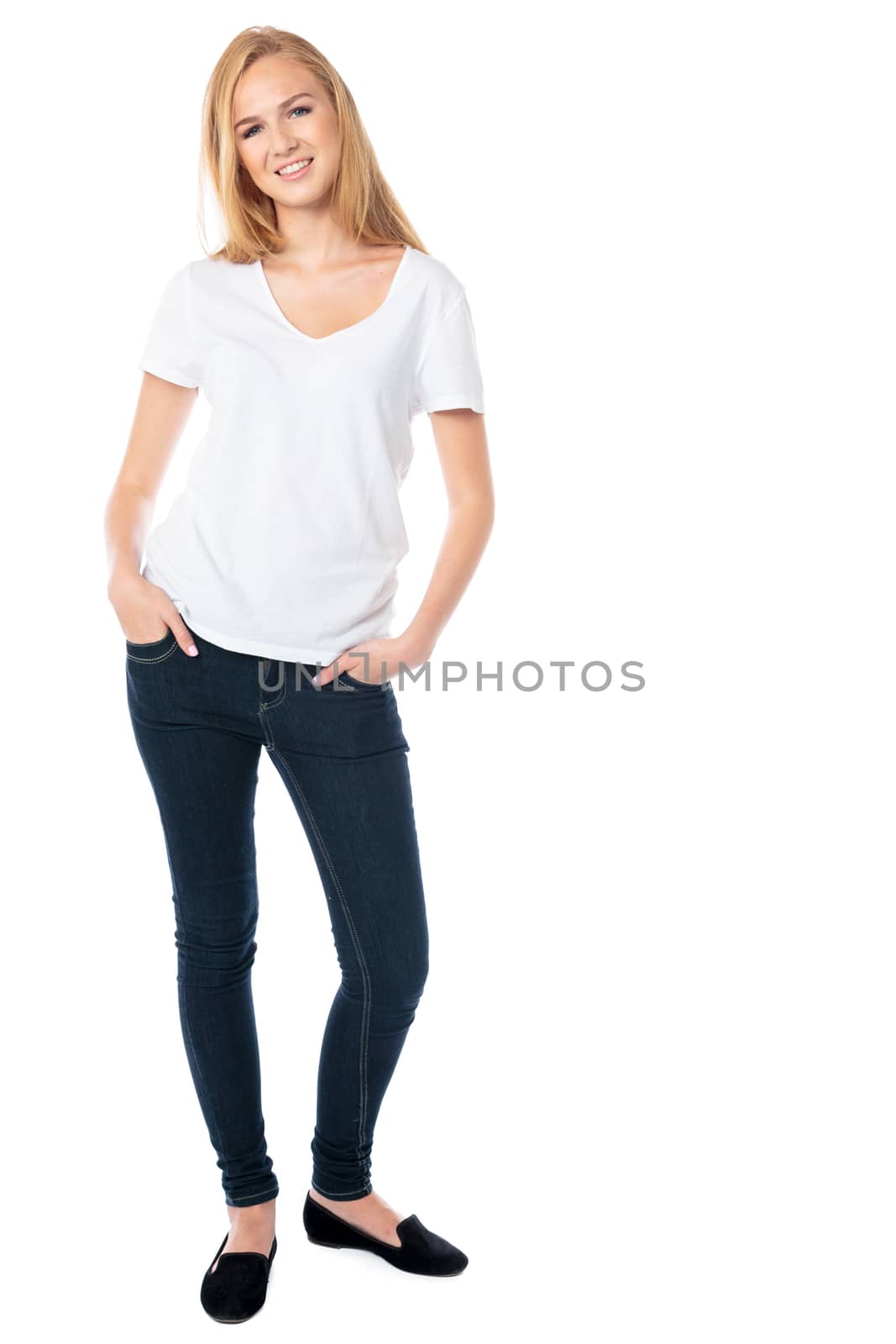 Attractive smiling woman with long blond hair in jeans standing with her hands in her pockets looking at the camera, isolated on white